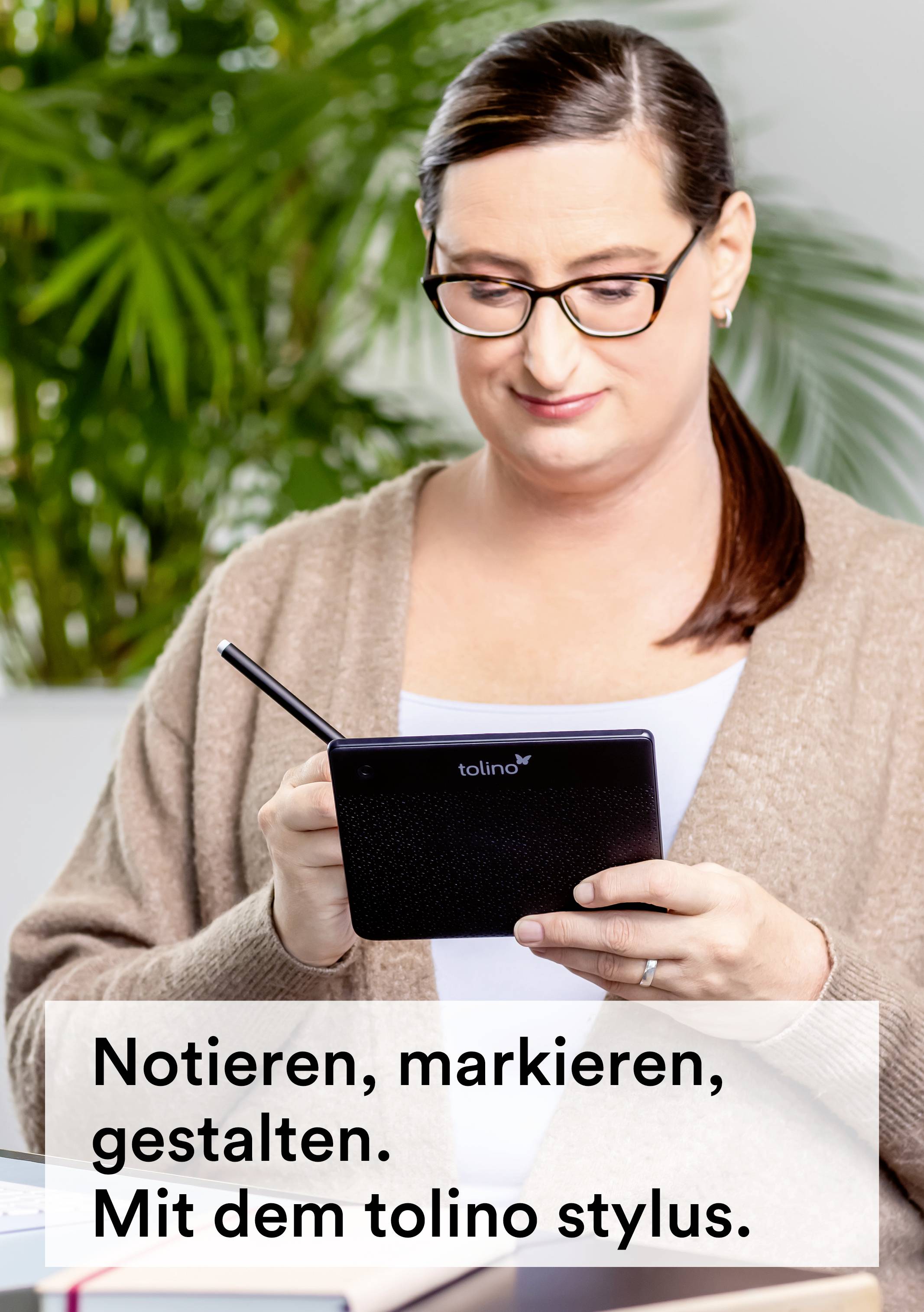 Een persoon zit en gebruikt een tolino Stylus om aantekeningen te maken of tekst te markeren. Op de achtergrond zijn planten zichtbaar.