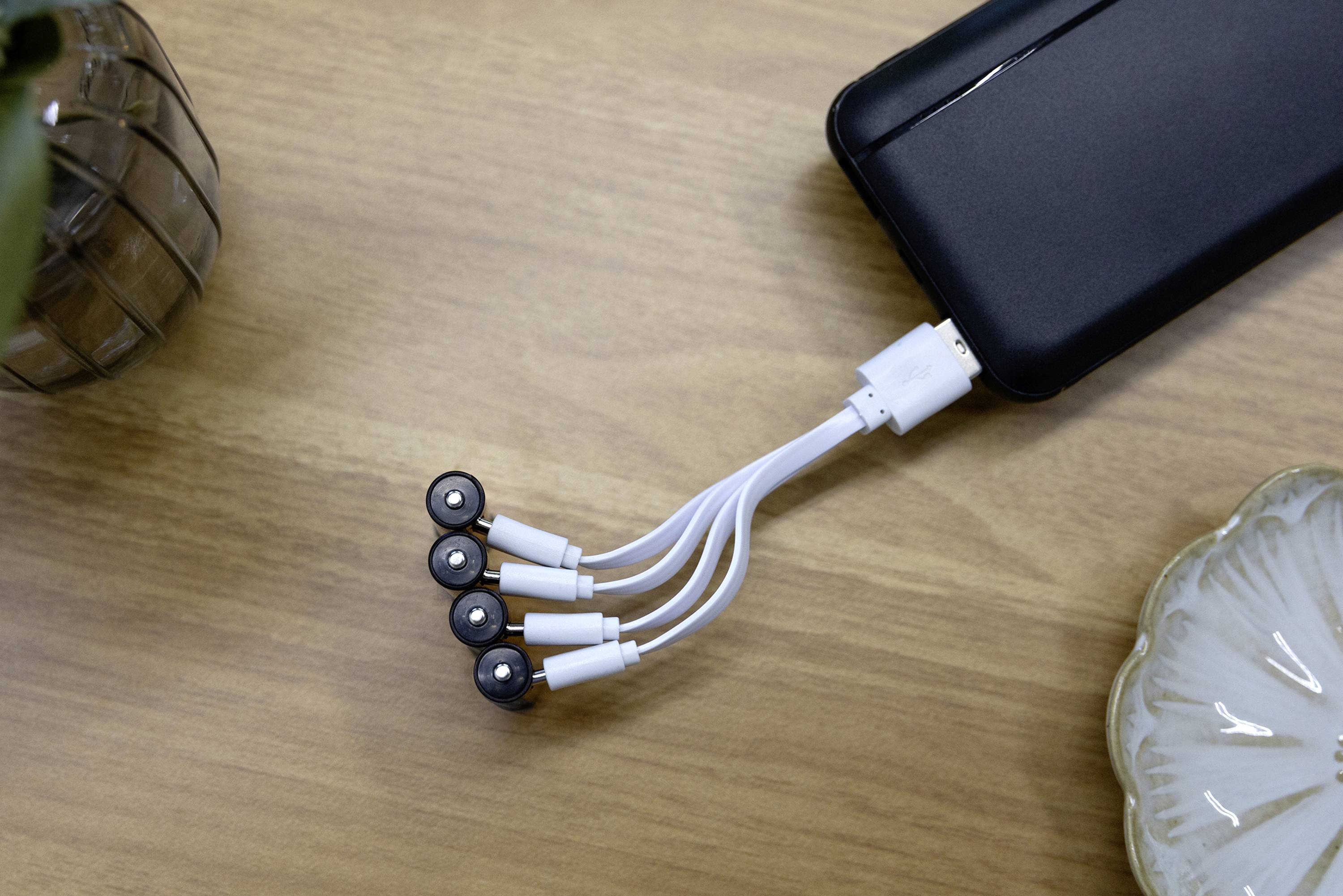 Een powerbank met meerdere witte oplaadkabels ligt op een houten tafel. De uiteinden van de kabels hebben magnetische aansluitingen.