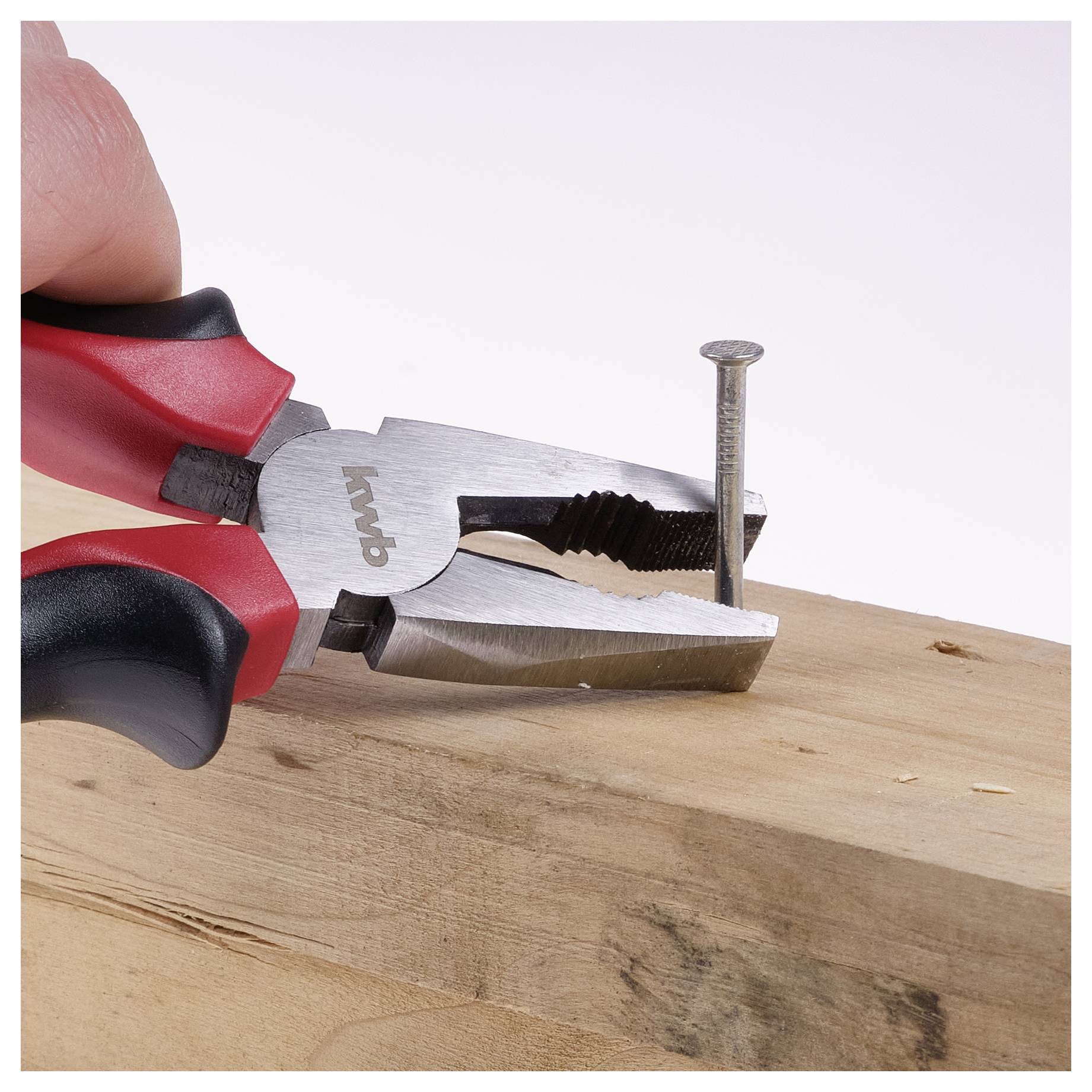 Een paar rode en zwarte tangen worden gebruikt om een spijker vast te houden die gedeeltelijk in een stuk hout is geslagen.