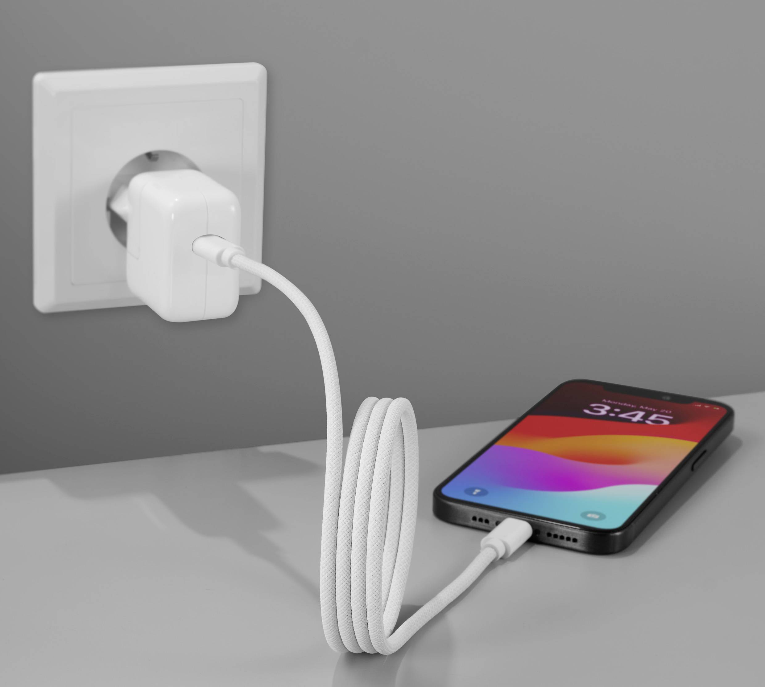 Een smartphone wordt met een oplaadkabel aangesloten op een stopcontact aan de muur. Het display toont de tijd 3:46.