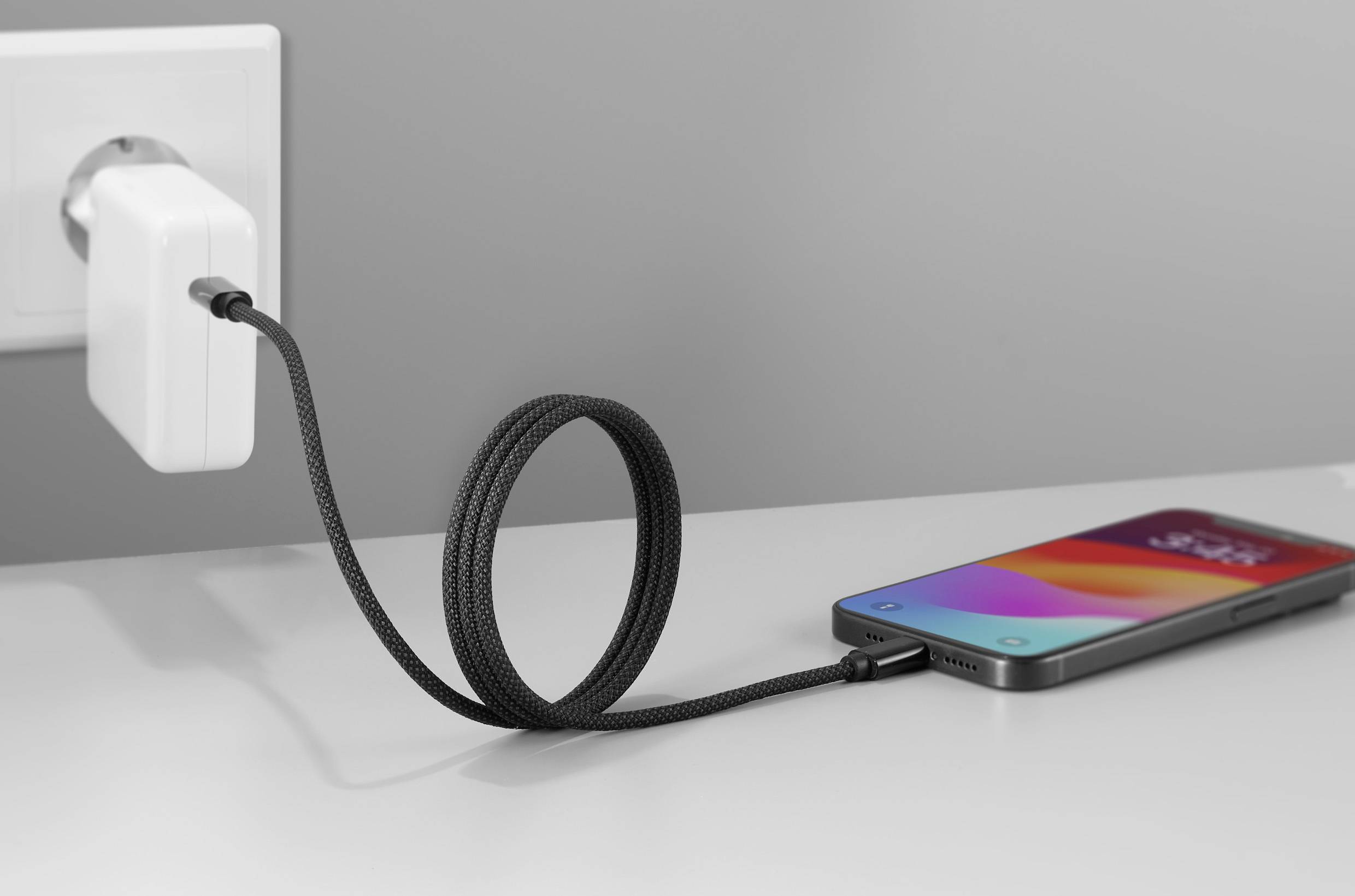 Een smartphone ligt op een tafel en wordt opgeladen via een kabel die is aangesloten op een stopcontact.