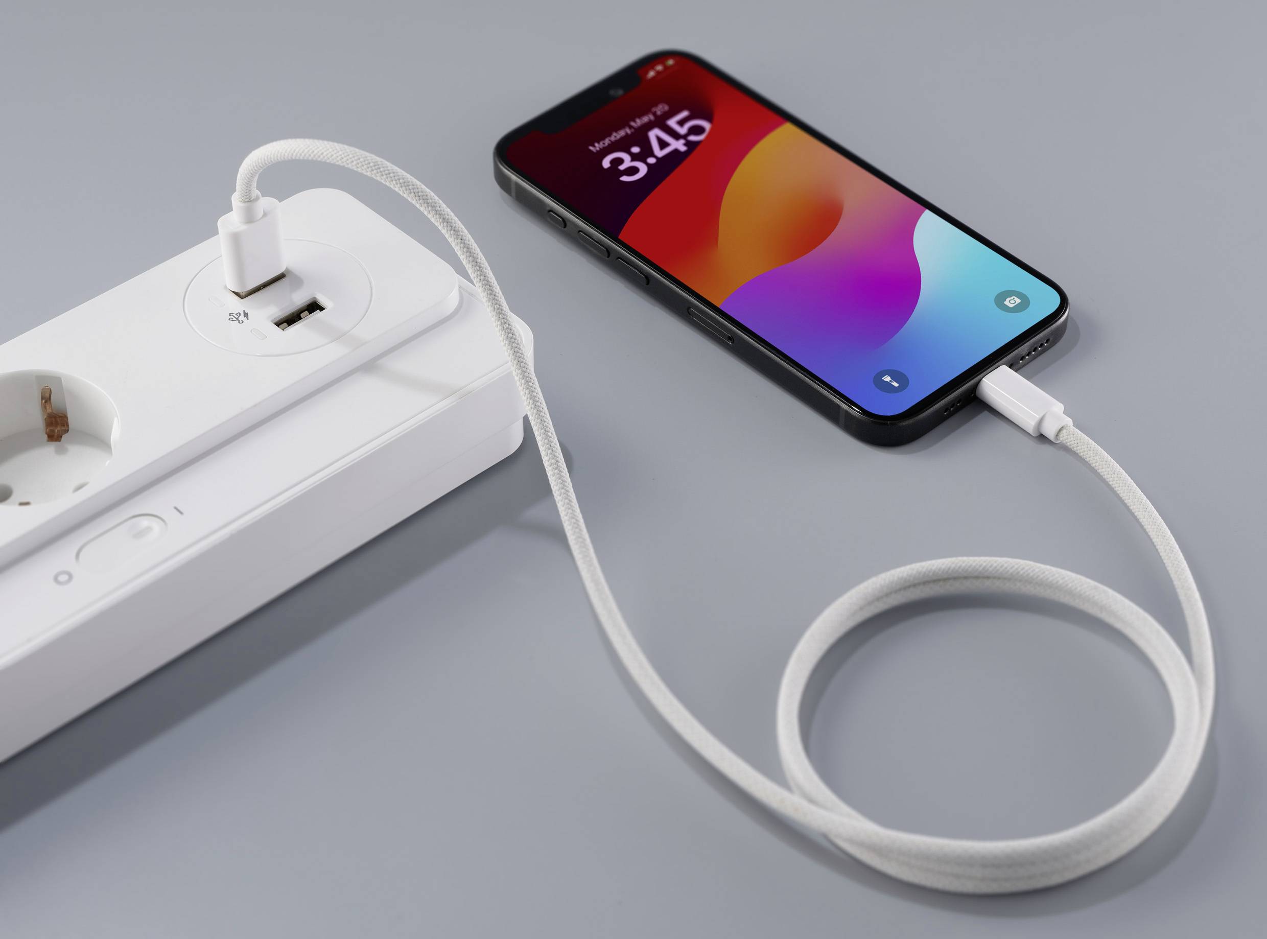 Smartphone met oplaadsymbool is via een USB-kabel aangesloten op een stekkerdoos. Het display toont de tijd 3:45.
