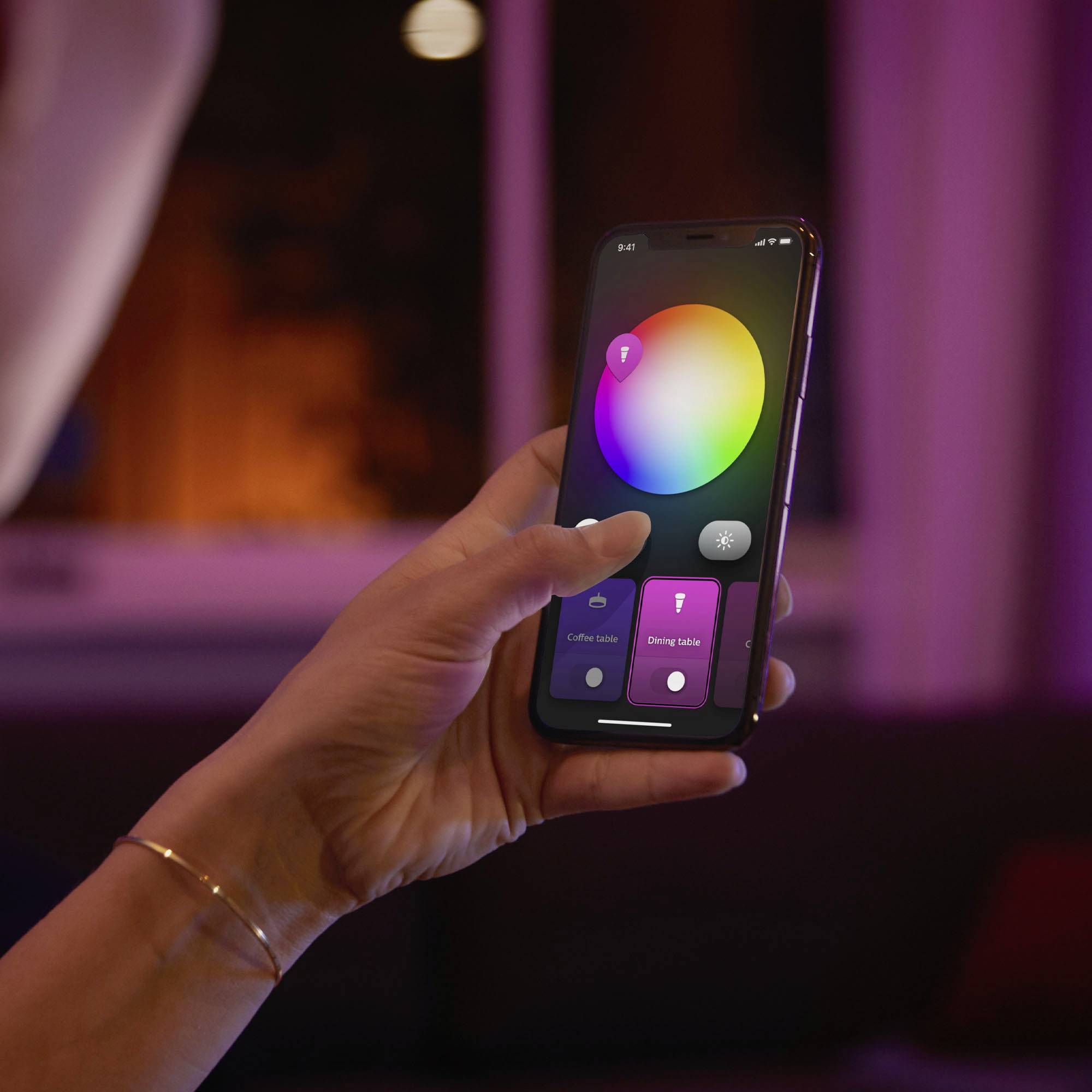 Een hand houdt een smartphone vast met een app voor het bedienen van kleur- en verlichtingsinstellingen. Paars licht op de achtergrond.