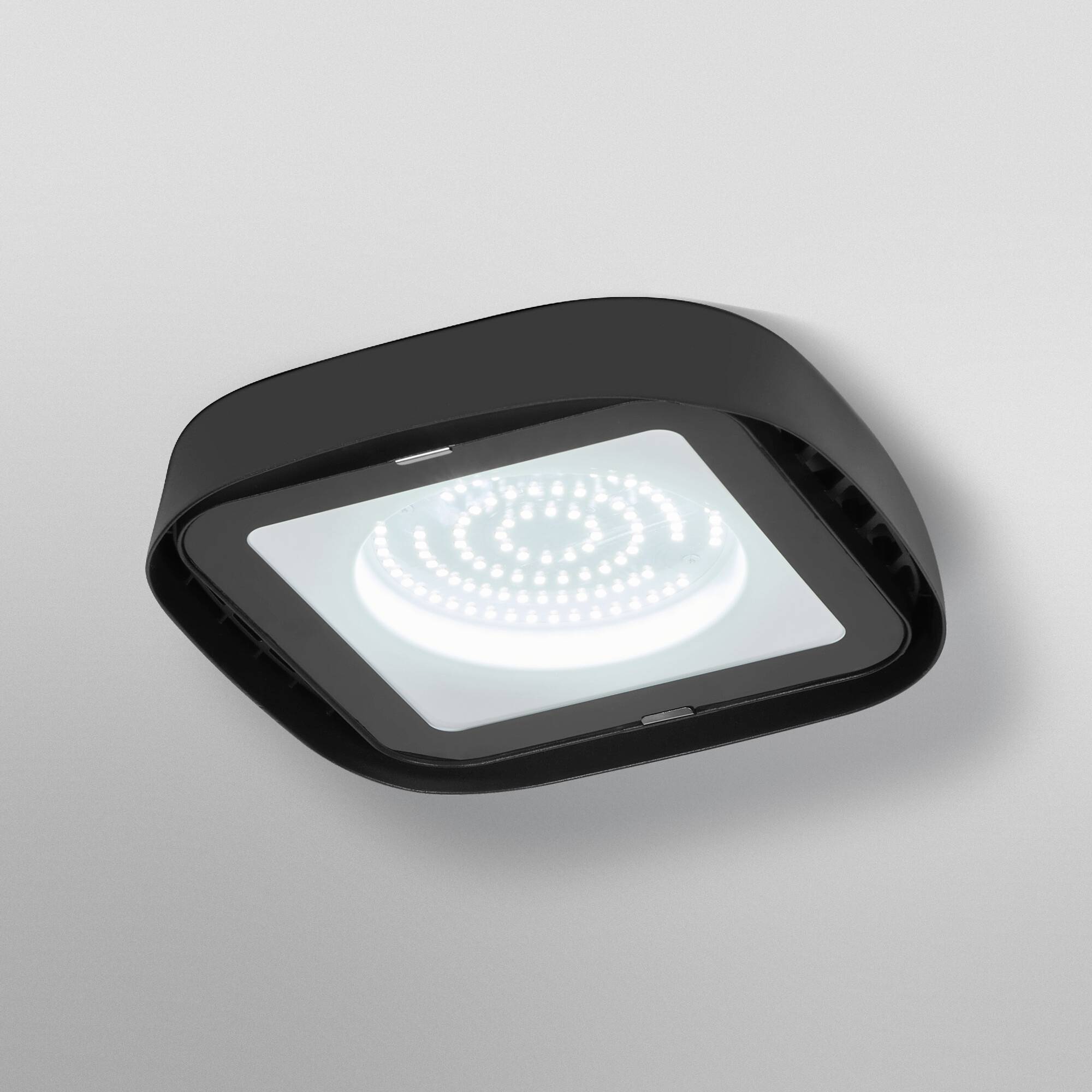 Een moderne, vierkante plafondlamp met een zwart frame en een verlicht LED-paneel, gemonteerd aan een grijze plafond.