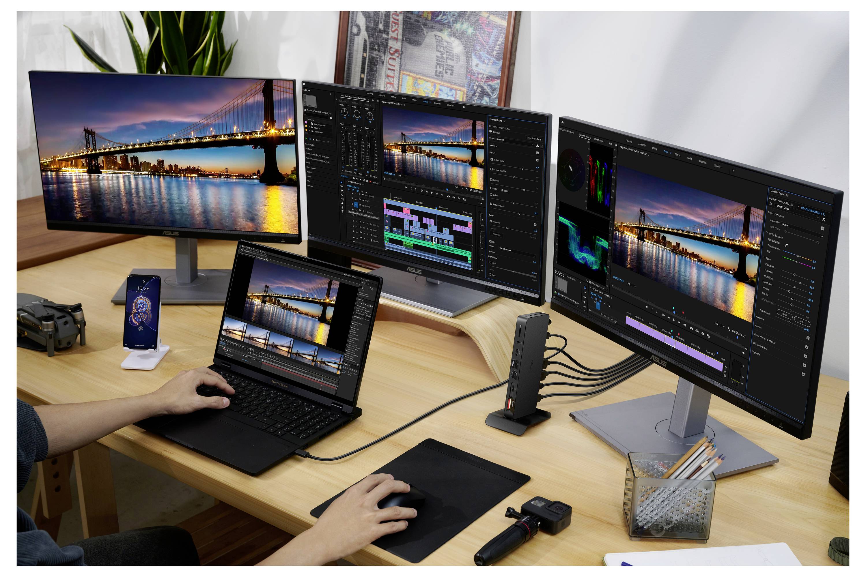 Meerdere monitors tonen een videobewerkingsprogramma met een brug bij nacht. Een gebruiker werkt op een laptop.