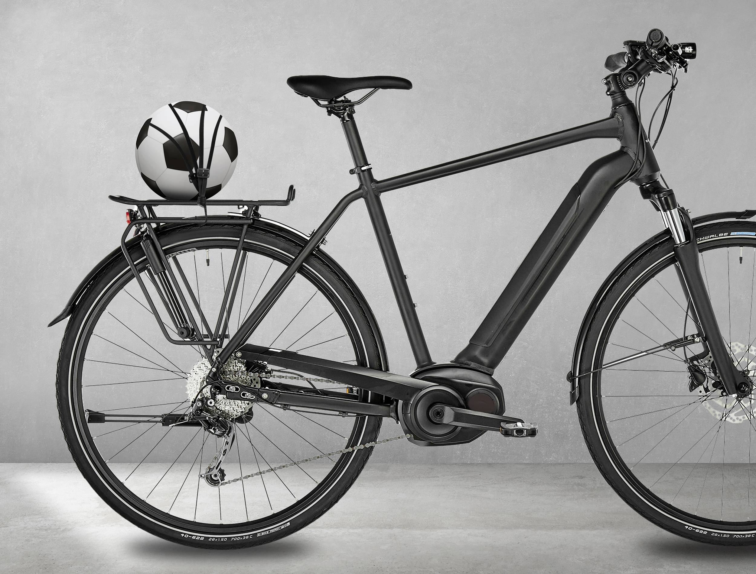 Zwarte elektrische fiets met een gewatteerde zitting en een balhouder aan de achterdrager, met een voetbal erin. Staat voor een grijze achtergrond.