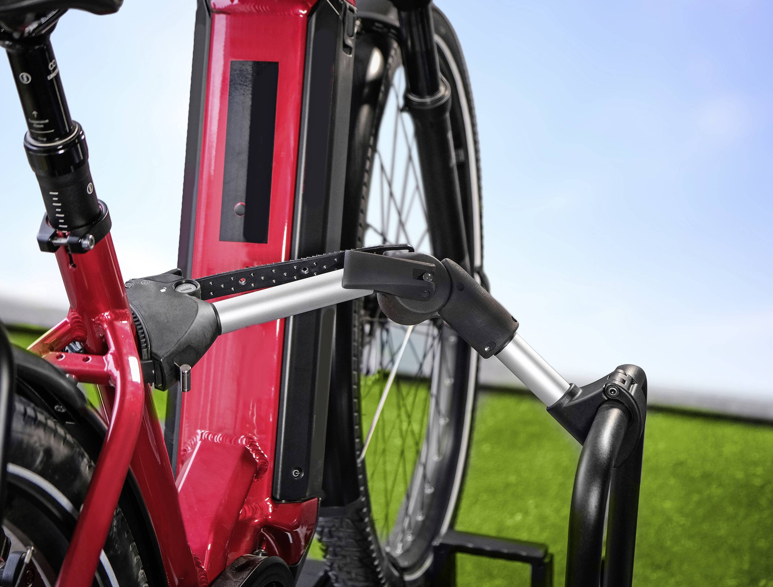 Rode elektrische fiets in een standaard met geïntegreerd fietsenslot, op een groene grasveld achtergrond onder een blauwe lucht.