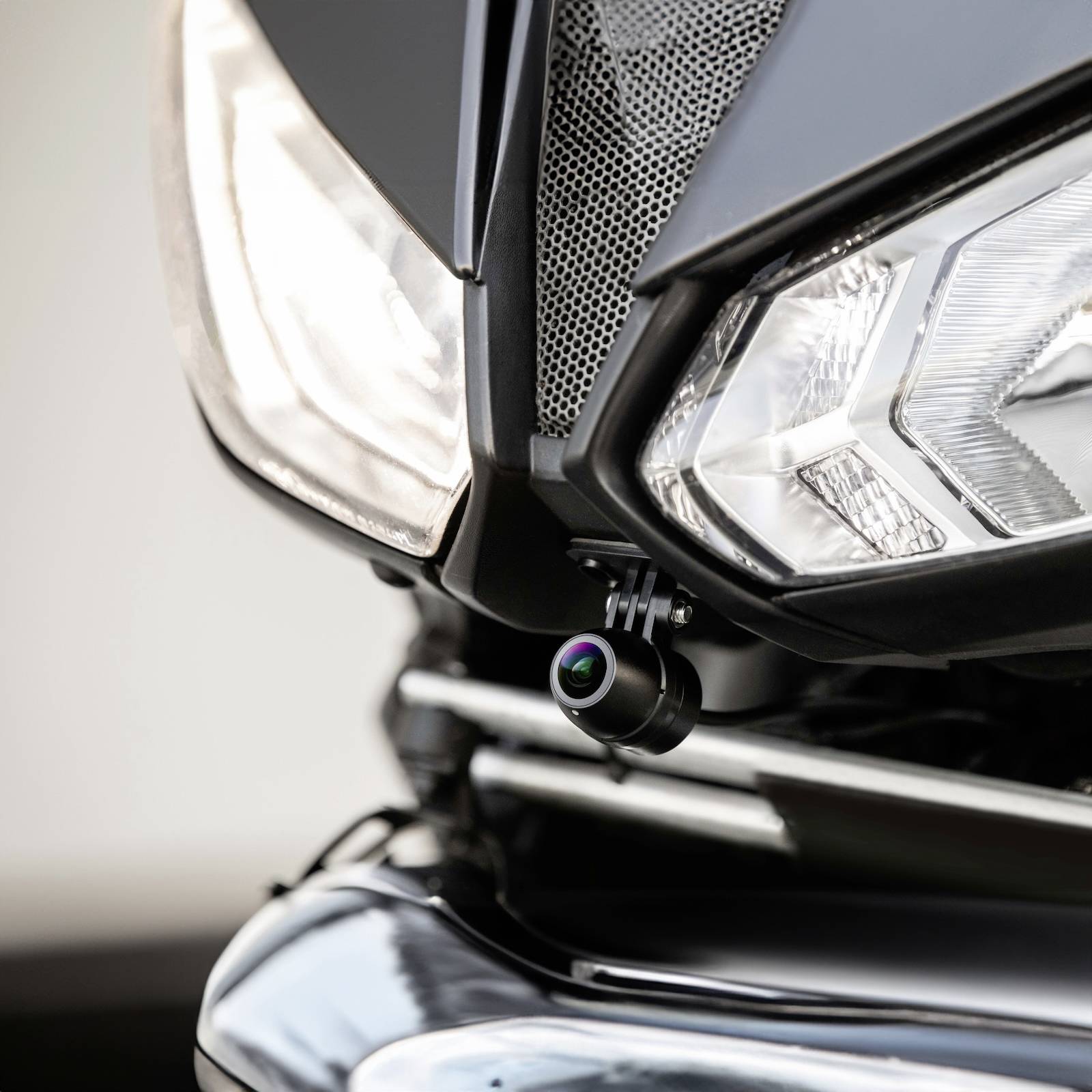 Close-up van een motorfiets-koplamp met een camera gemonteerd eronder, die wordt gebruikt voor veiligheid of opname.