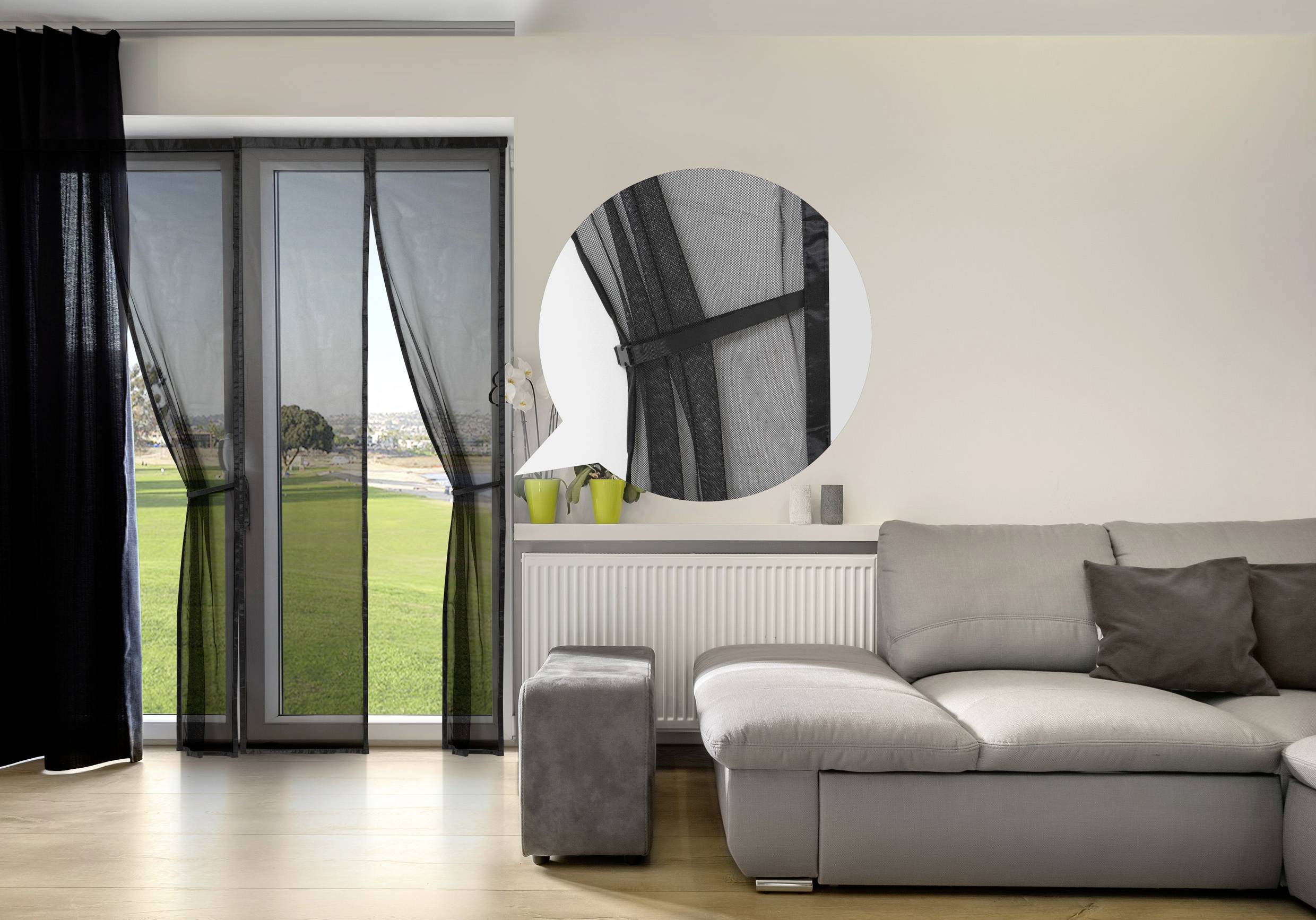 Een woonkamer met een grijze bank, zicht op een tuin door een glazen deur met zwarte gordijnen, gedetailleerd aanzicht van de deurscharnieren.