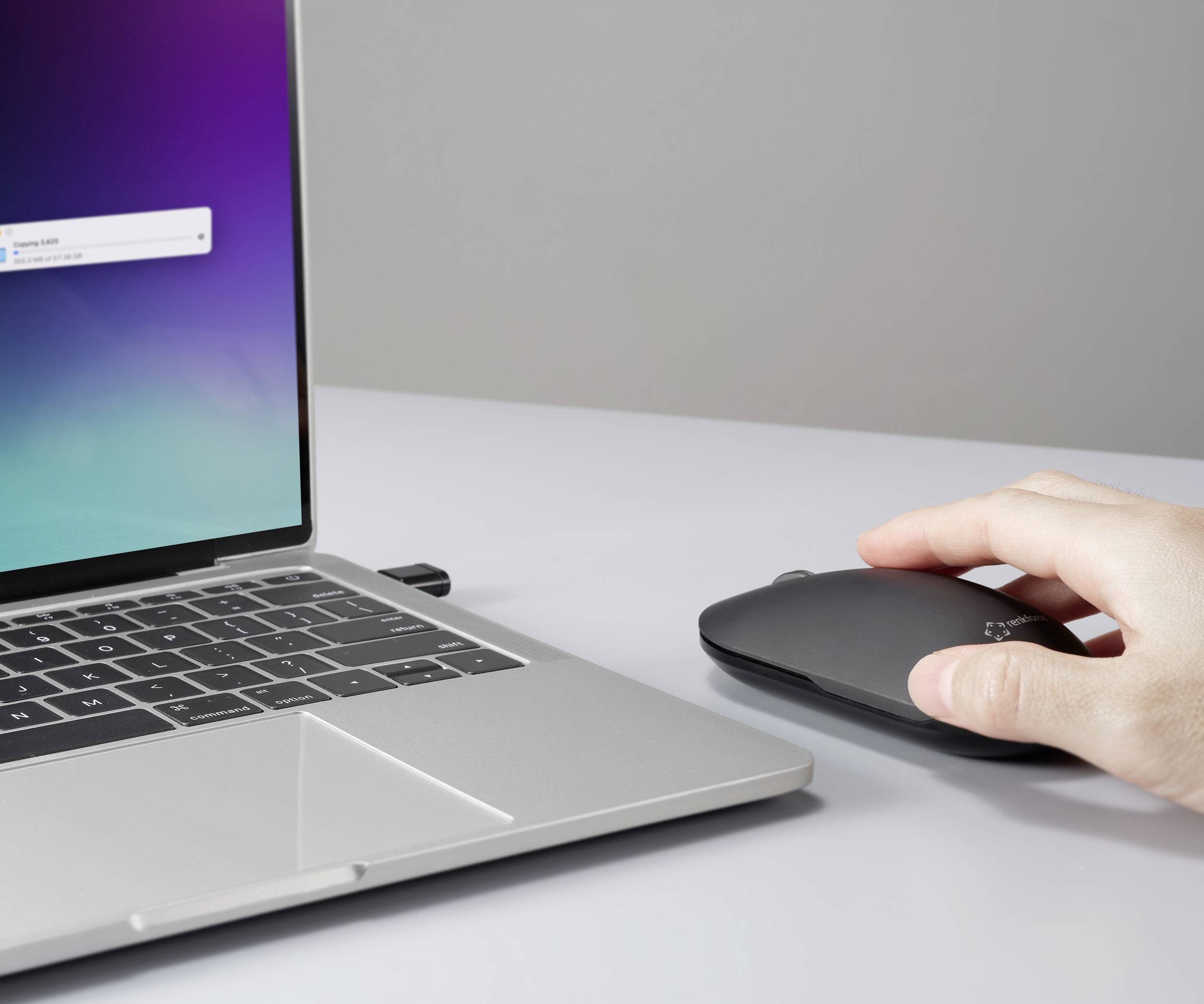 Hand beweegt een draadloze muis naast een laptop. De laptop toont een melding op een blauwe achtergrond.