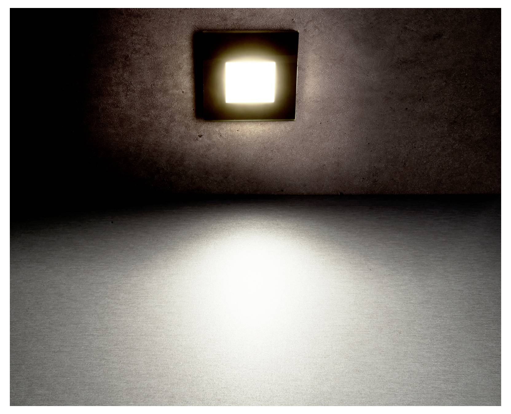 Een schemerige kamer met een heldere vierkante wandlamp die een gloed op de vloer werpt.