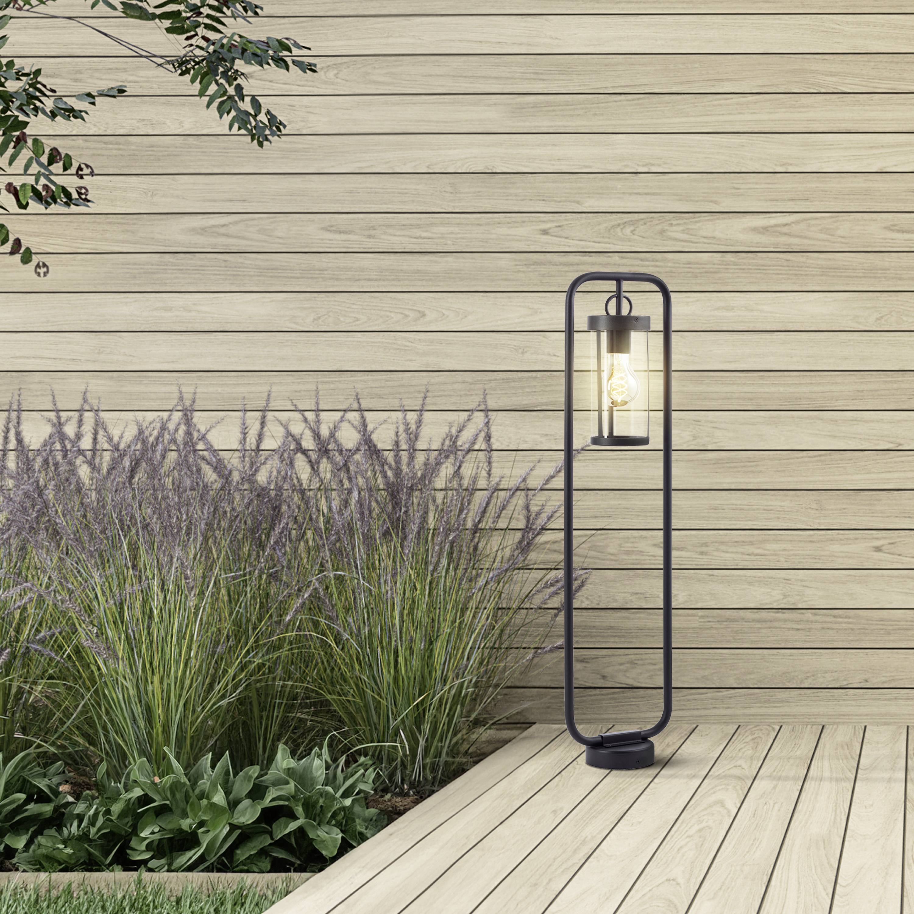 Groene grassen groeien naast een moderne staande lamp voor een houten wand. Een rustige, minimalistische tuinscène.