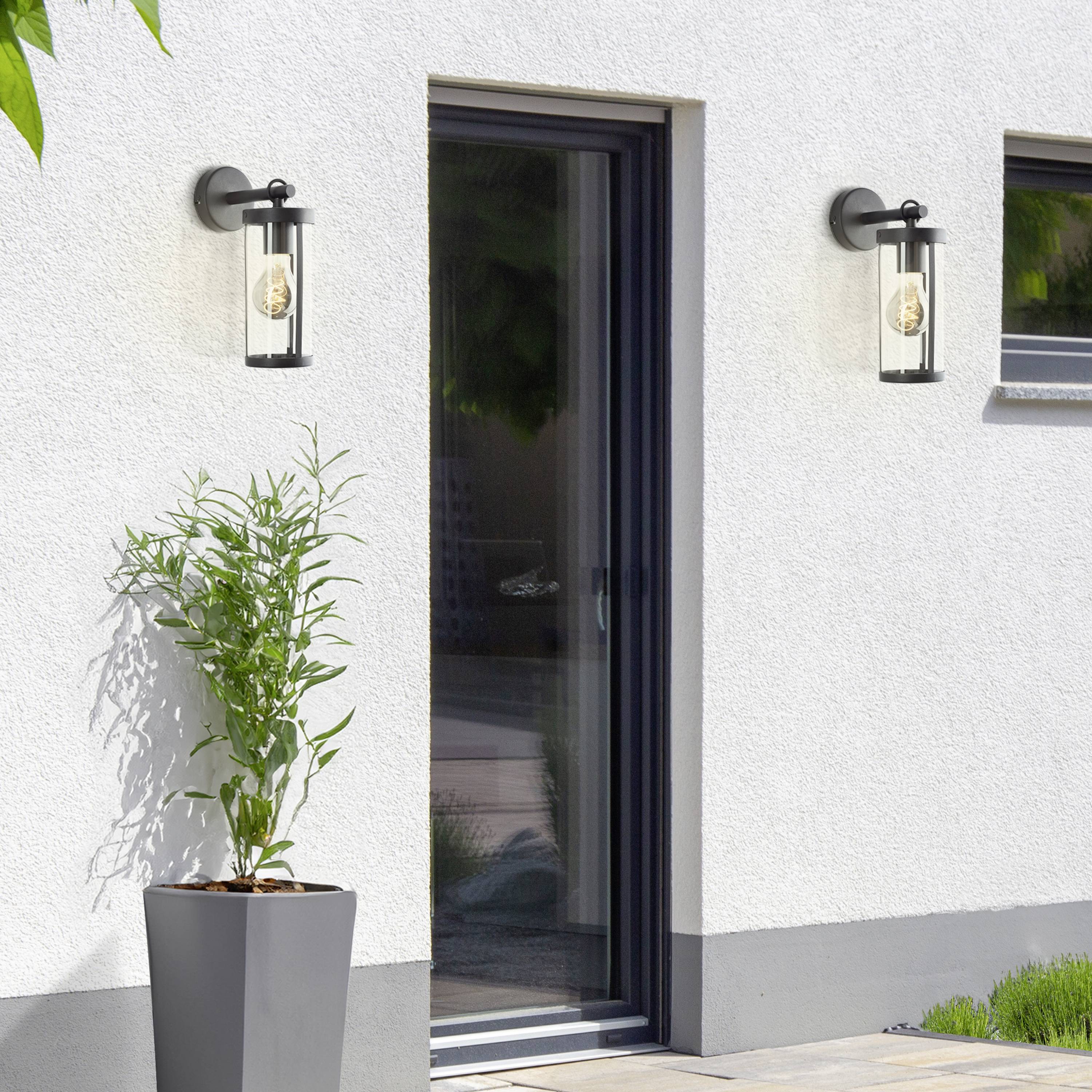 Een moderne entree van een huis, geflankeerd door twee buitenwandlampen. Een grote plantenpot met een groene struik staat links.