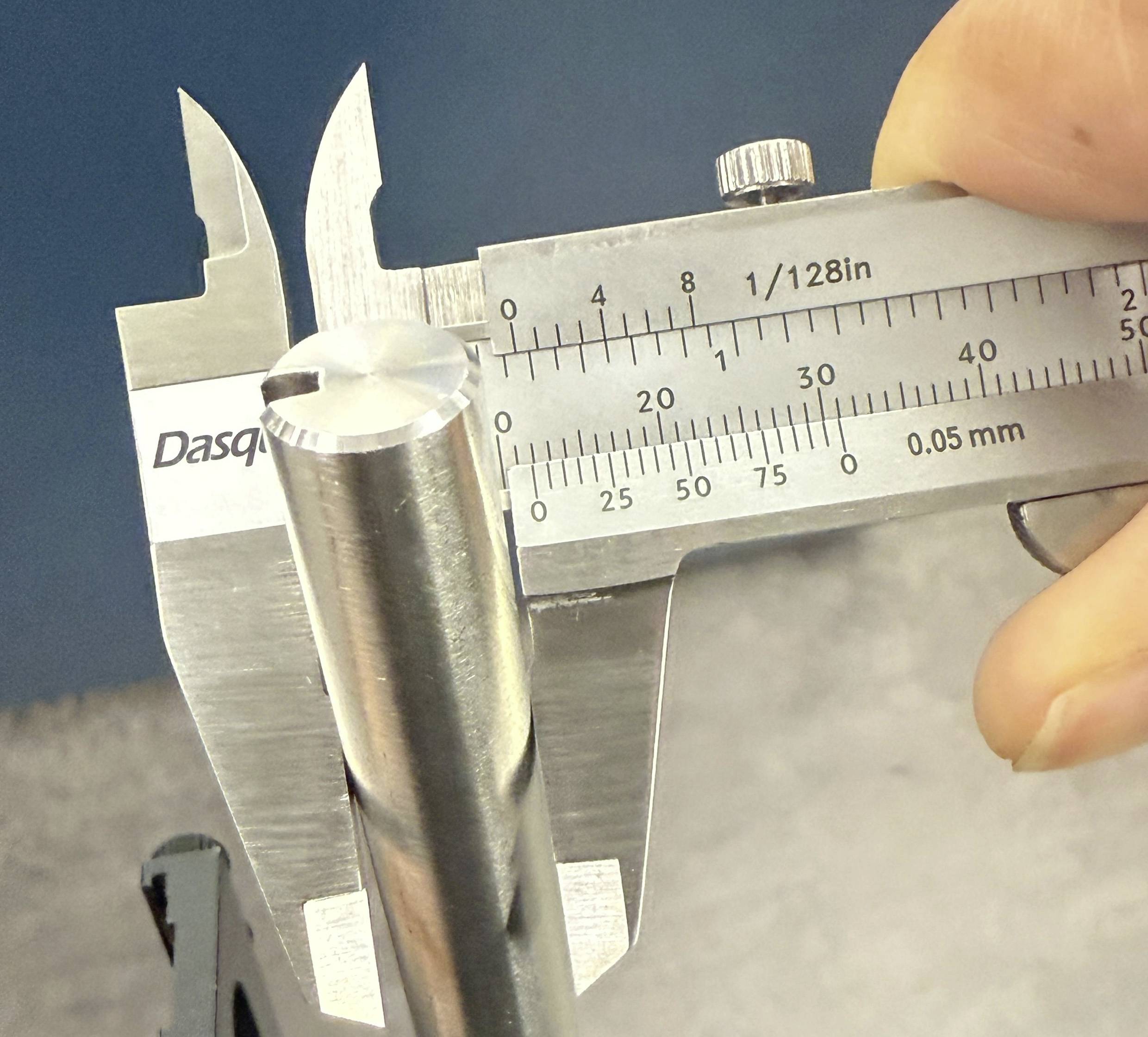 Een hand houdt een schuifmaat vast aan een metalen cilinder. De schaal toont een meting in inches en millimeters.