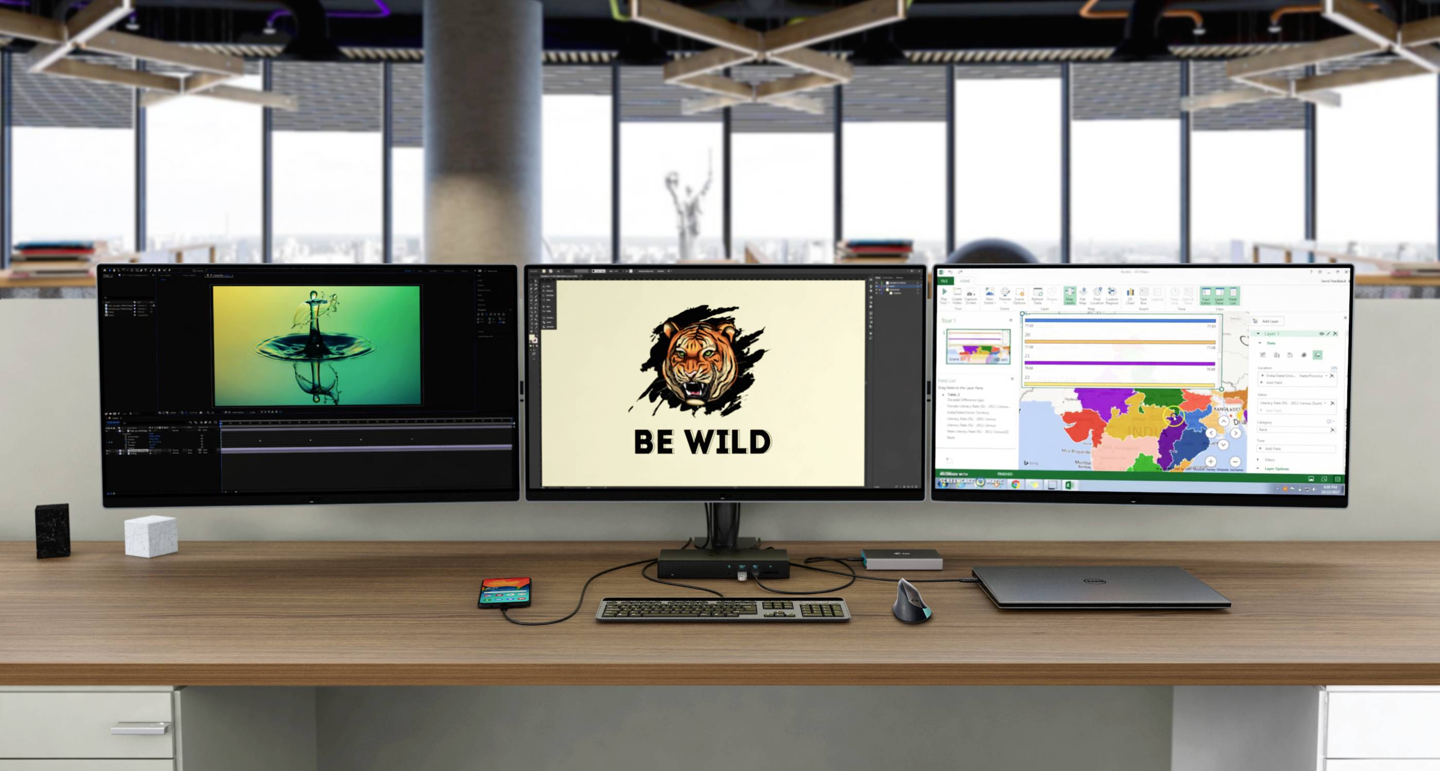 Drie computermonitoren op een bureau tonen van links naar rechts: een grafisch programma, een afbeelding met 'Be Wild', en een gekleurde kaart.