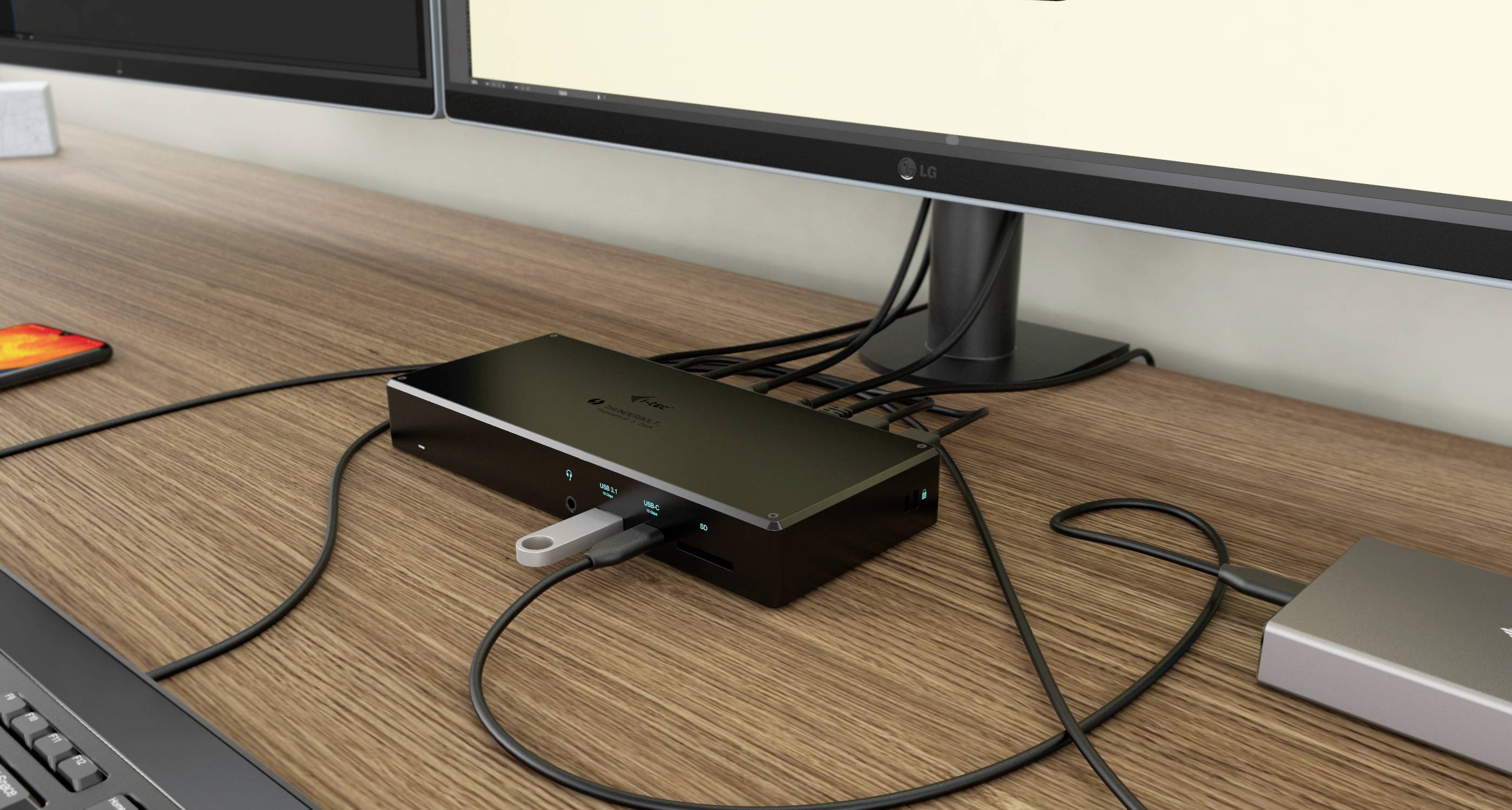 Een bureau toont een computerscherm, een USB-hub met een USB-stick aangesloten en meerdere verbonden kabels.
