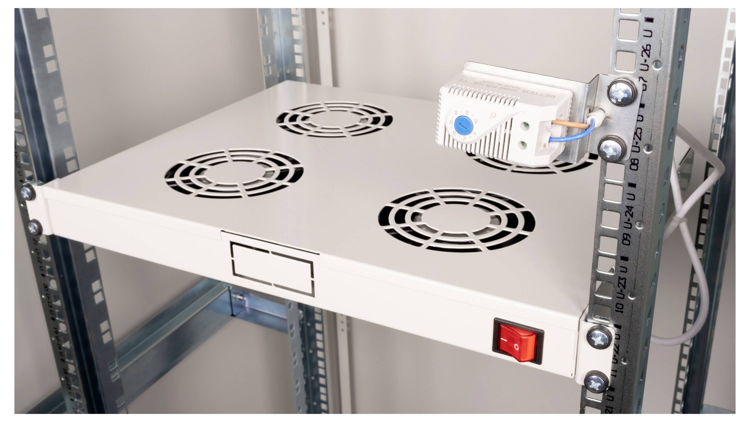 Een rek met ventilatierooster en een daaraan gekoppeld elektrisch apparaat. Een rode schakelaar is aan de voorkant bevestigd.