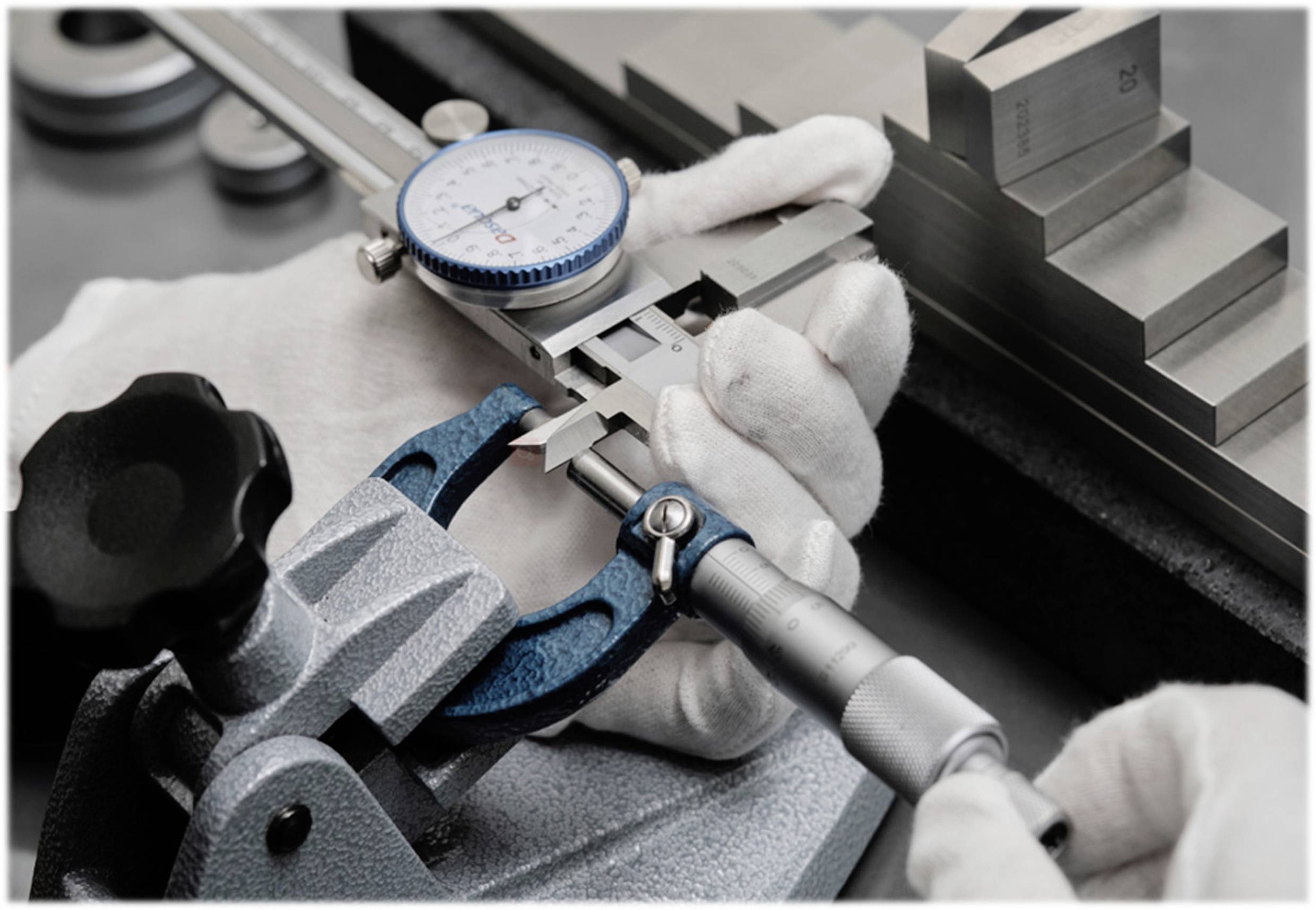 Close-up van handen in witte handschoenen die een meetinstrument vasthouden tegen een metalen blok om de precisie te controleren.