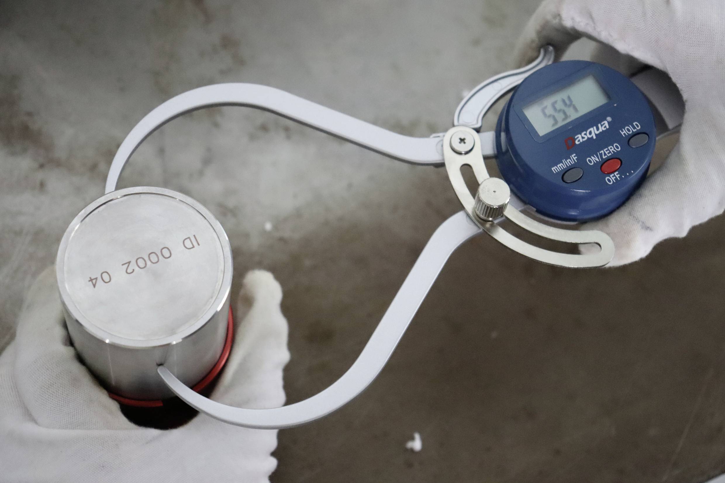 Een persoon meet de diameter van een cilindrisch metalen onderdeel met een schuifmaat. De meetwaarde geeft '5.54' aan.