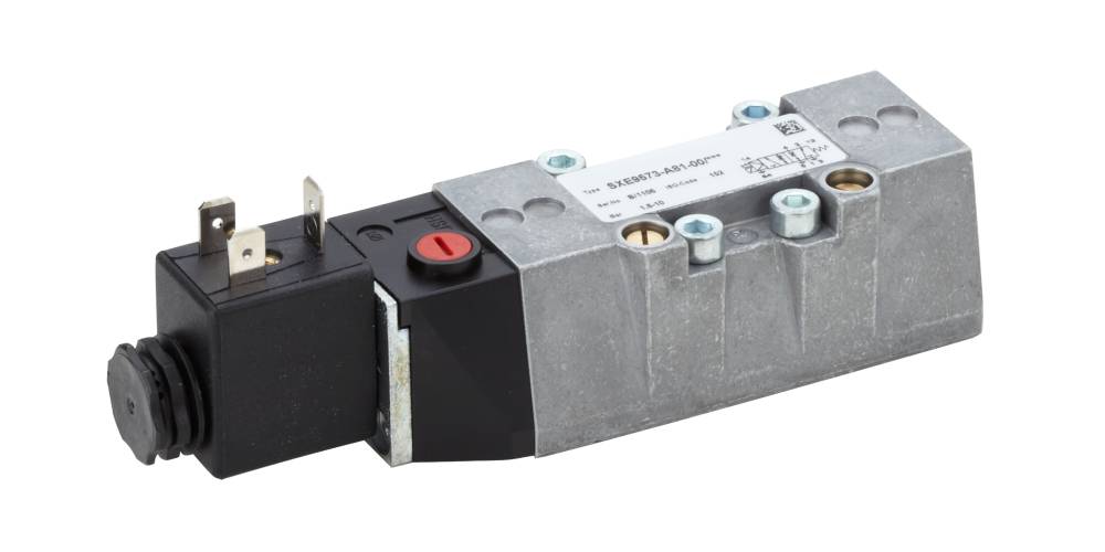 Een zilveren elektromagnetisch ventiel met zwarte en rode toetsen, metalen aansluitingen en opschriften op de bovenkant.