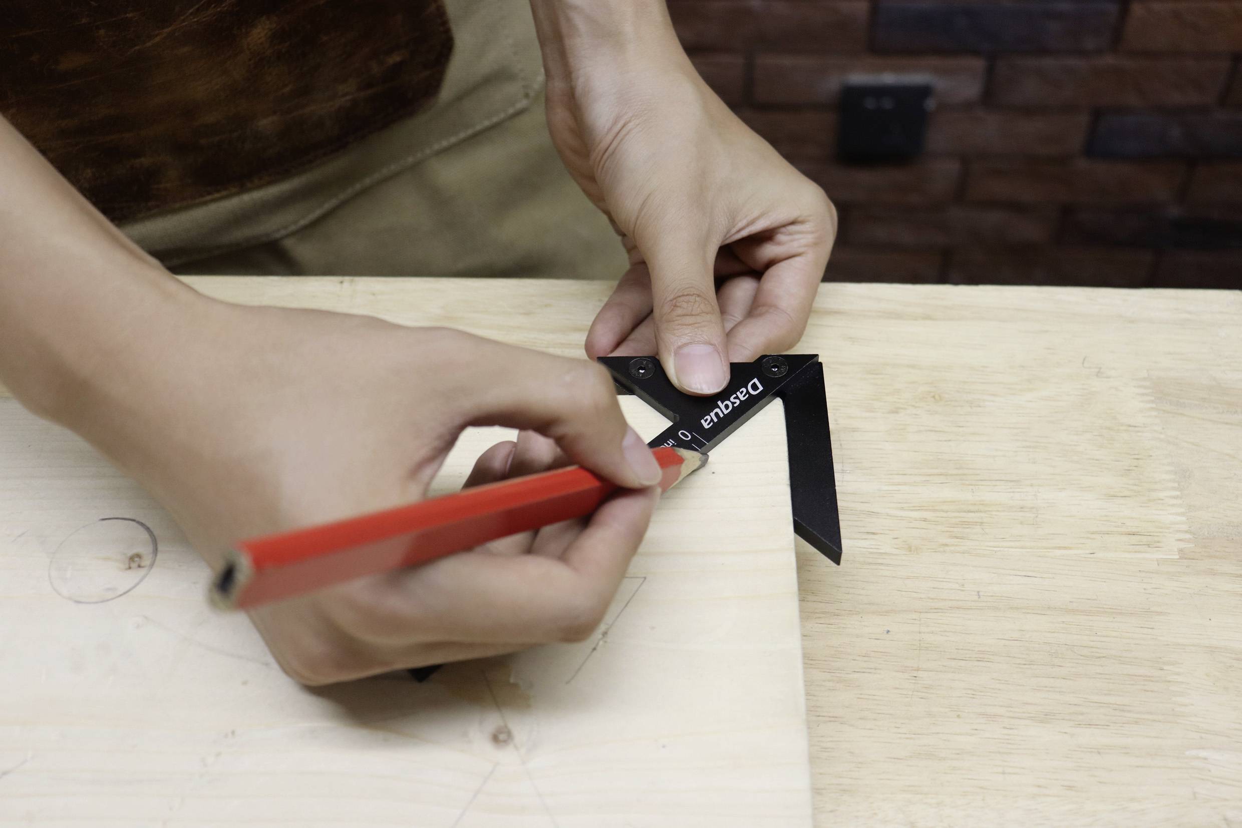 Een persoon gebruikt een timmermanshaak en een rode potlood om nauwkeurige markeringen op een houten plank te tekenen.
