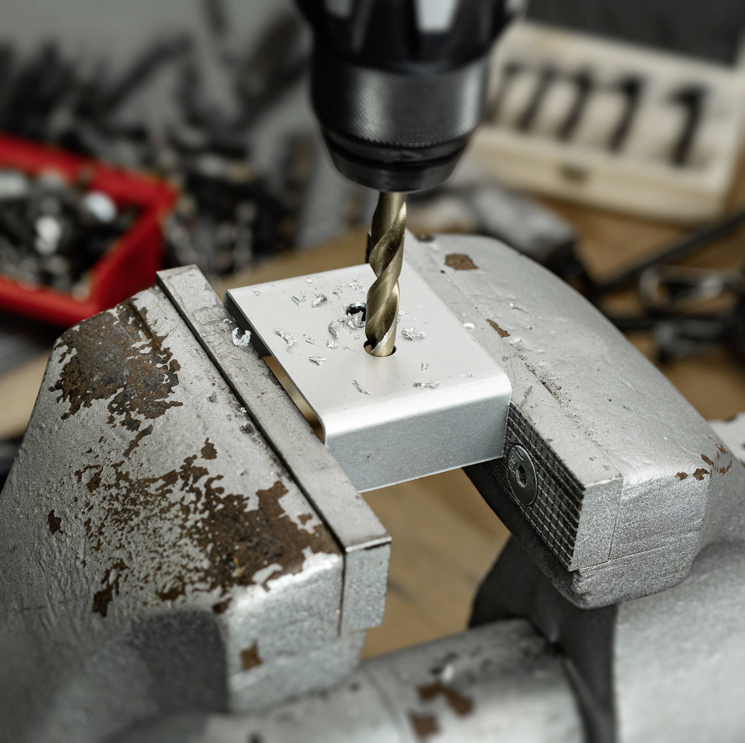 'Een boor maakt een gat in een metalen stuk dat in een bankschroef op een werkbank is vastgezet.'