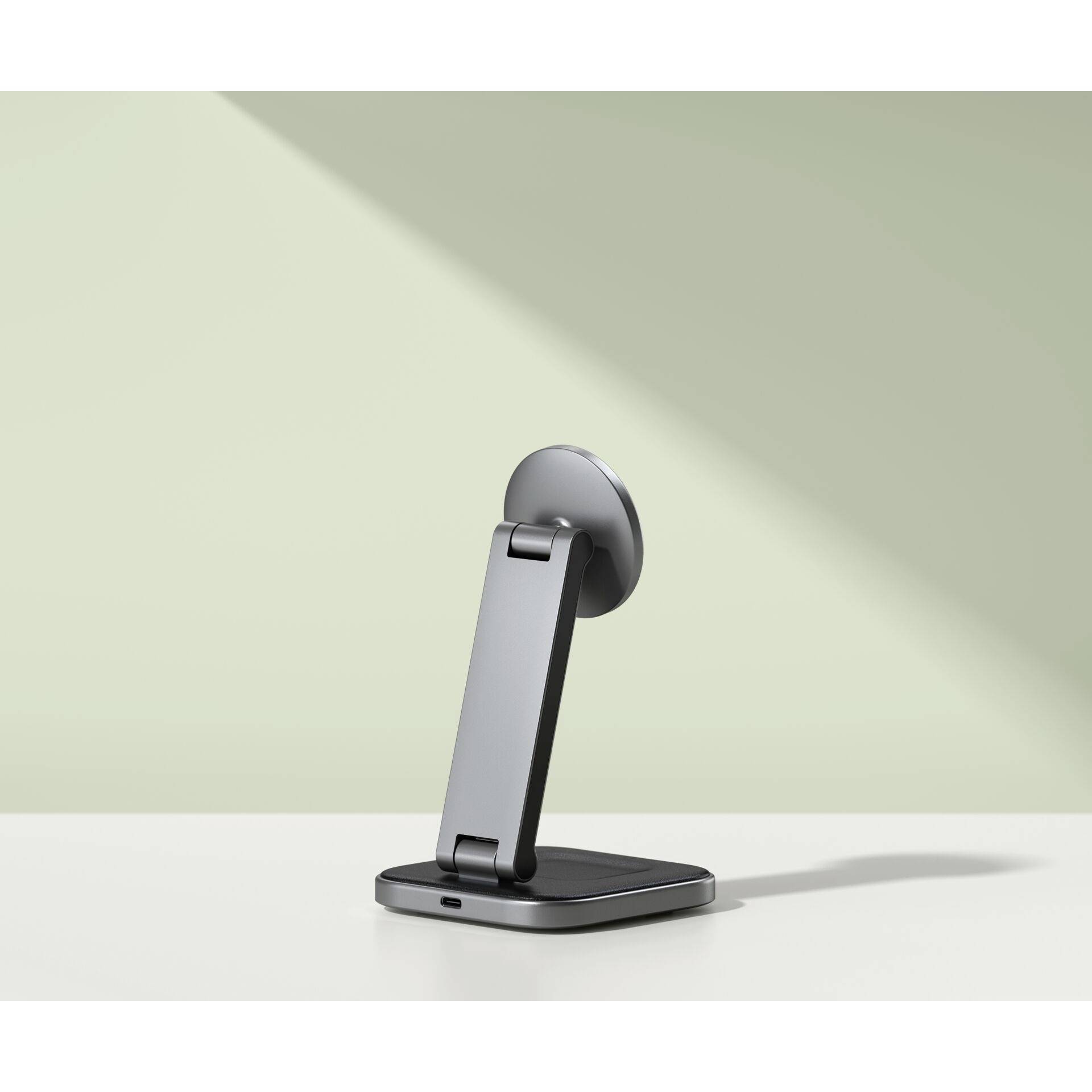 Een grijze telefoonhouder staat rechtop op een wit oppervlak voor een lichtgroene muur op de achtergrond.
