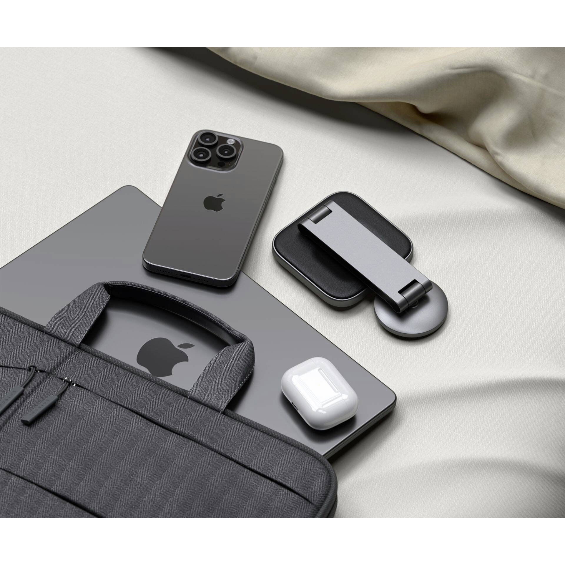 Laptop, smartphone, AirPods en toebehoren op een bed naast een zwarte tas. Tech-producten worden netjes gerangschikt weergegeven.