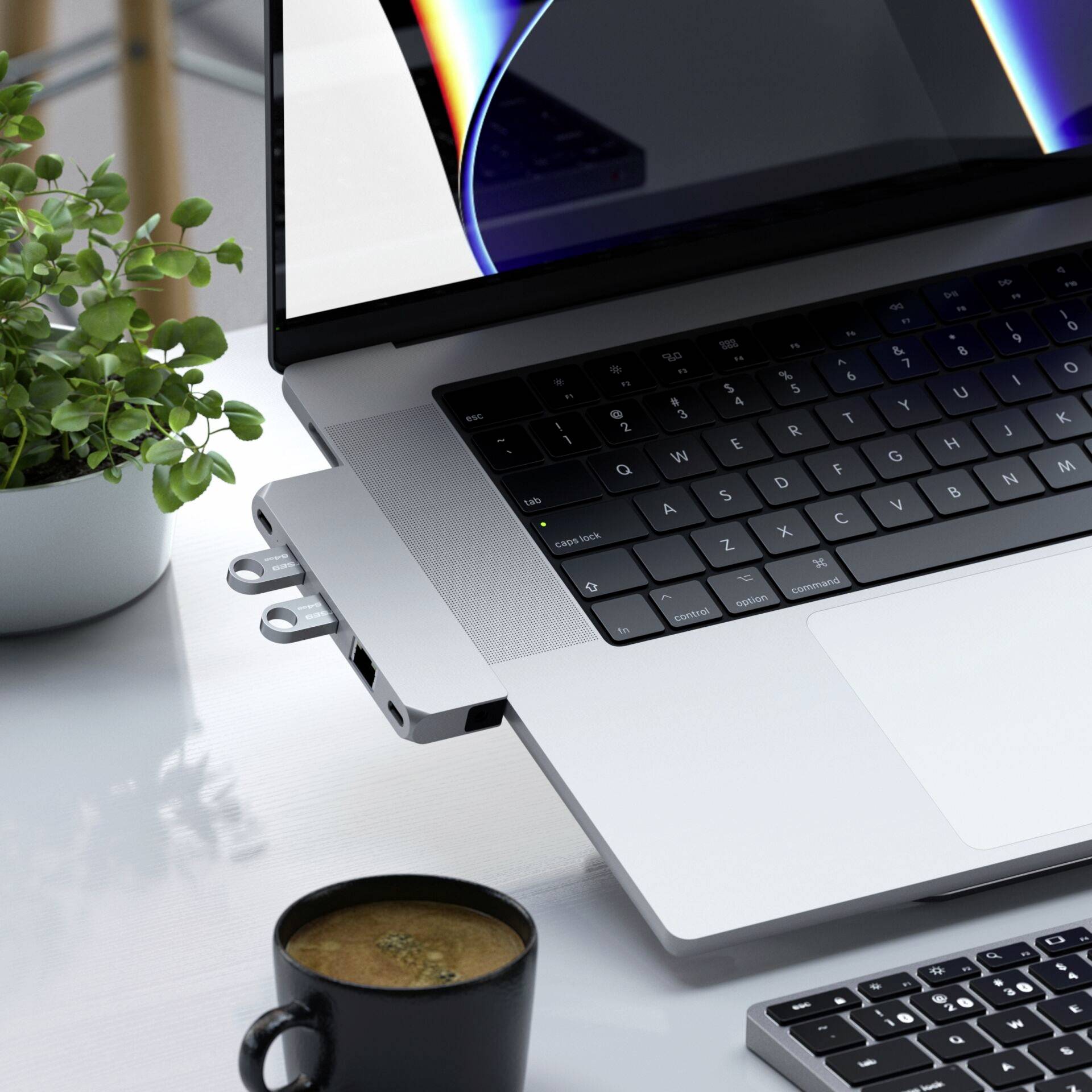 Een laptop op een bureau naast een kopje en een toetsenbord. Op het laptopscherm is een kleurrijk ontwerp te zien.