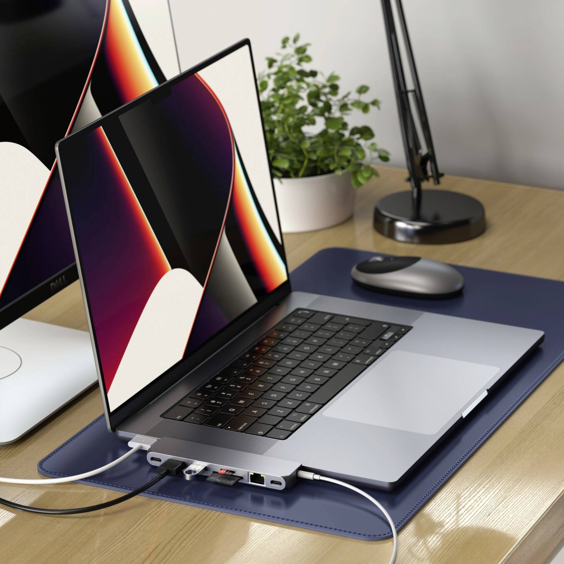 Een moderne laptop met toetsenbord en een groot scherm staat op een bureau. Ernaast een plant, een muis en een lamp.