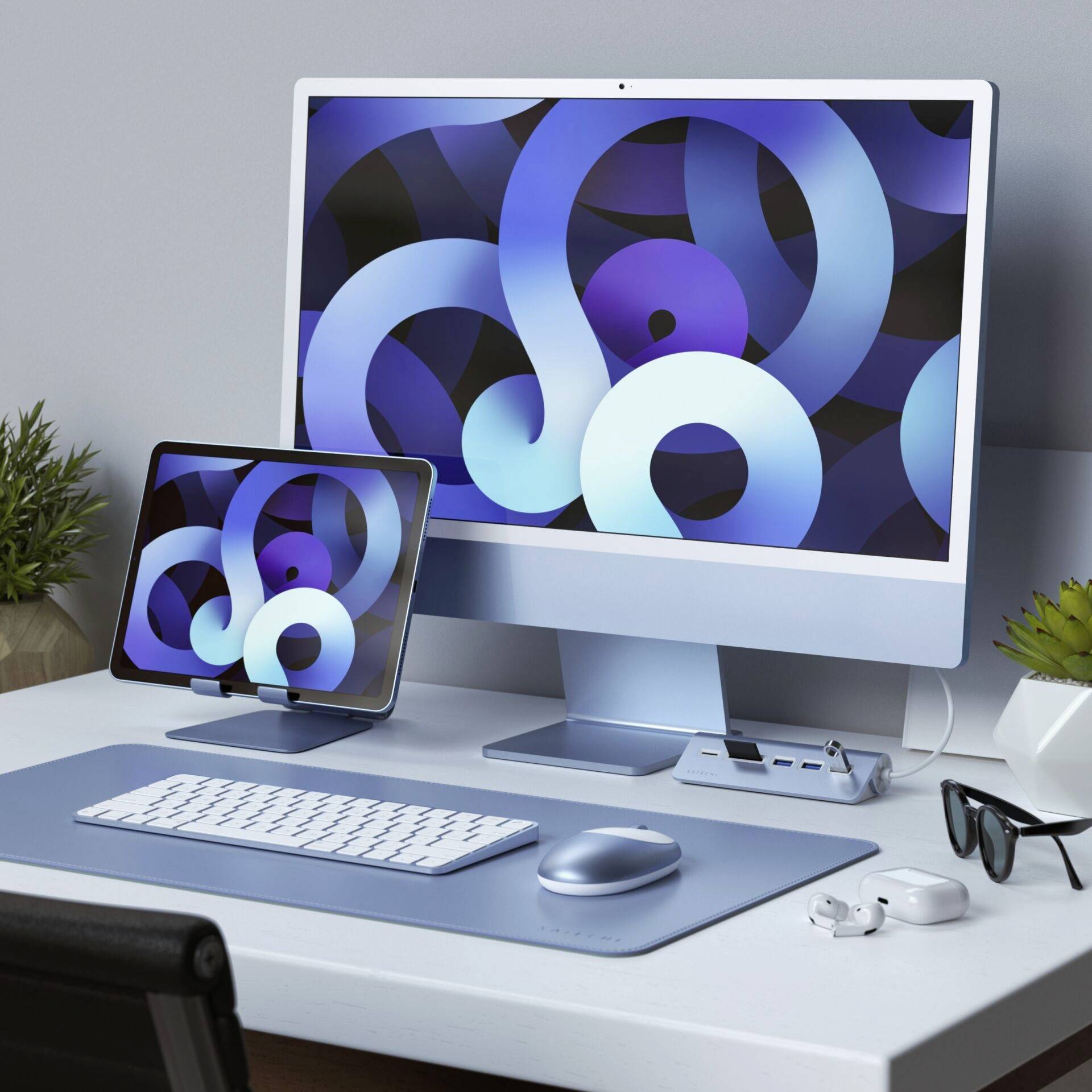 Moderne werkplek met desktopcomputer en tablet, beide vertonen abstracte, blauwe cirkelpatronen op het scherm. Wit accessoire op blauwe bureauondergrond.