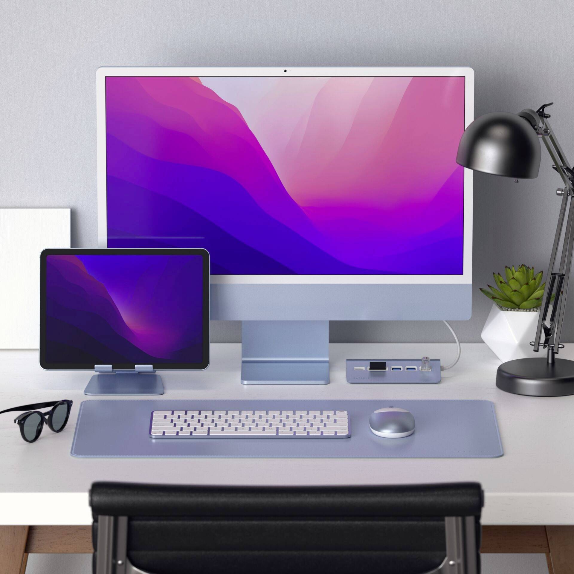 Een moderne bureautafel met een groot beeldscherm, een tablet ernaast, een toetsenbord en een muis. Rechts staan een lamp en een plant.