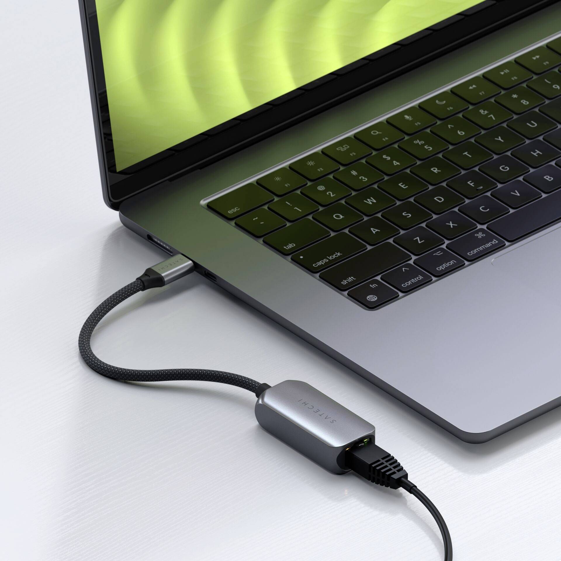 Een zilvergrijs laptoptoestel met een groen scherm is via een zwarte kabel verbonden met een USB-C-adapter.