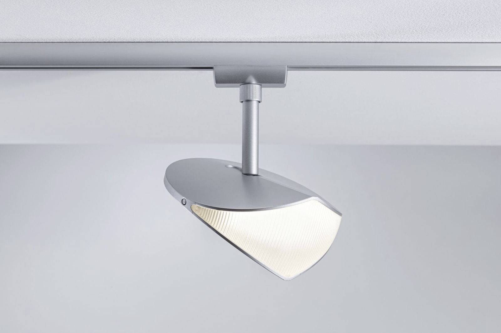 Een moderne plafondlamp met een zilveren, lensvormige kap die zacht licht naar beneden uitstraalt, gemonteerd op een rail.