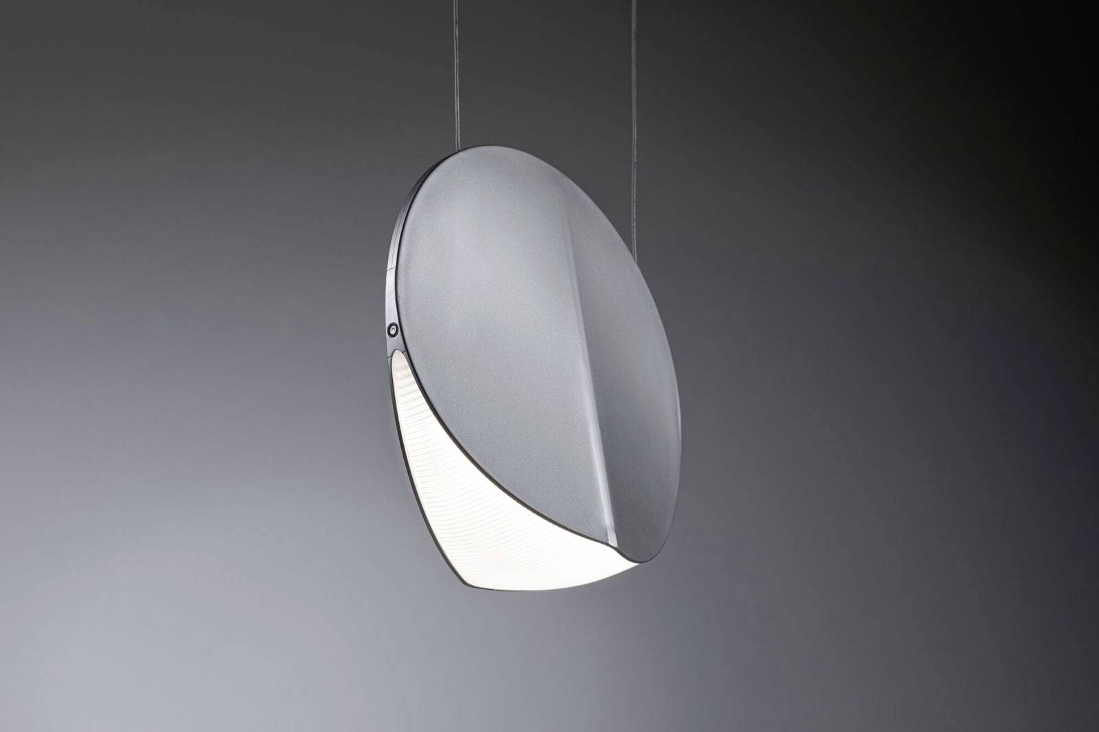 Een moderne, ronde hanglamp met een metaalgrijs afwerking en een halfmaanvormig lichtgebied, hangt zwevend in een donkere omgeving.