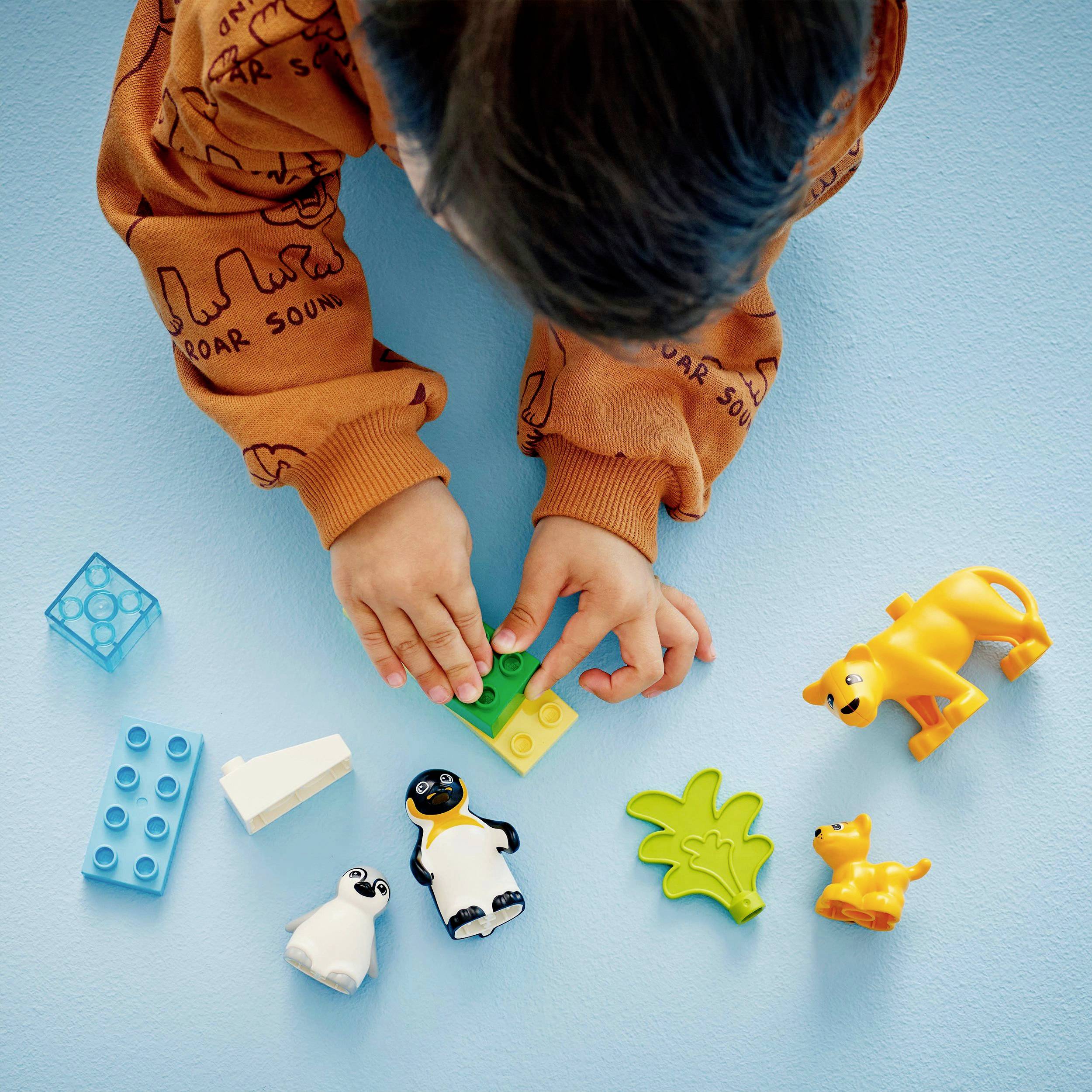 Een kind speelt op een blauwe ondergrond met kleurrijk speelgoed, waaronder Legoblokken en plastic dierfiguren.