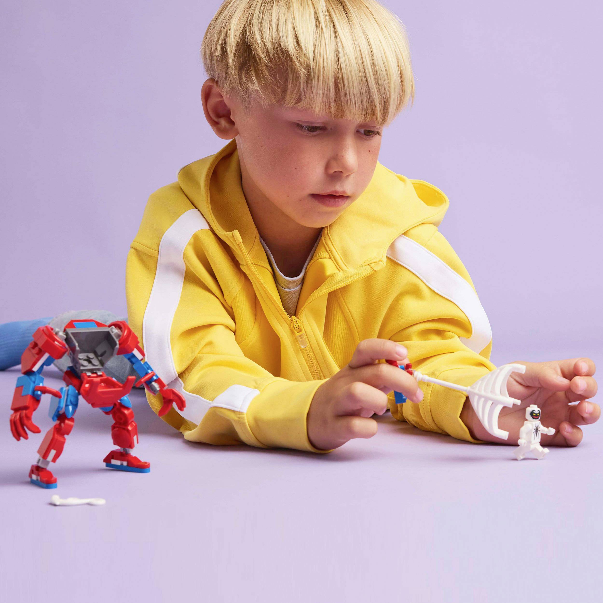Een kind speelt met een kleine witte robot en een grotere rode robot. Het kind draagt een gele trui.