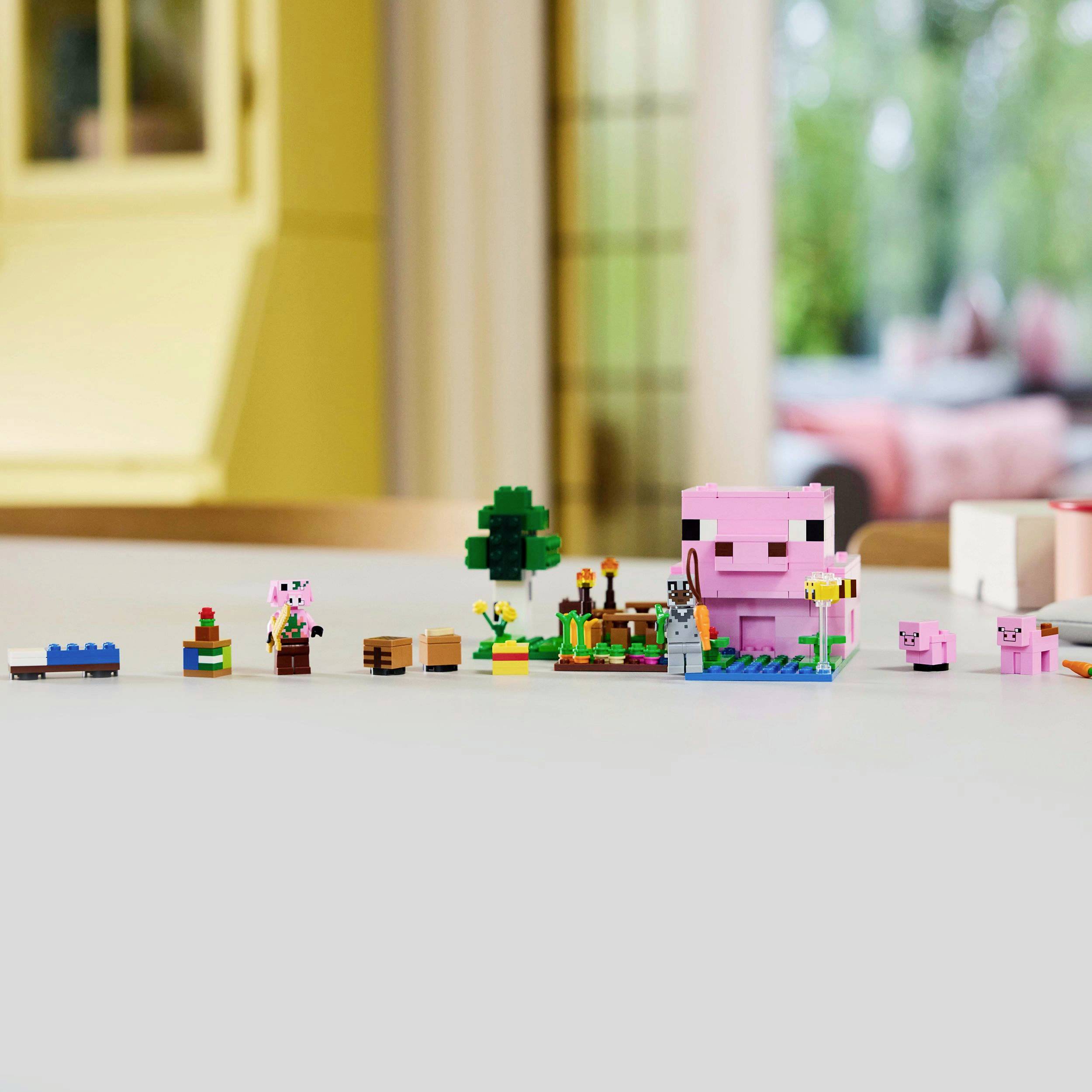 Een reeks kleine, gekleurde speelgoedfiguren en blokken is gerangschikt op een tafel, met op de achtergrond een wazig woonvertrek.