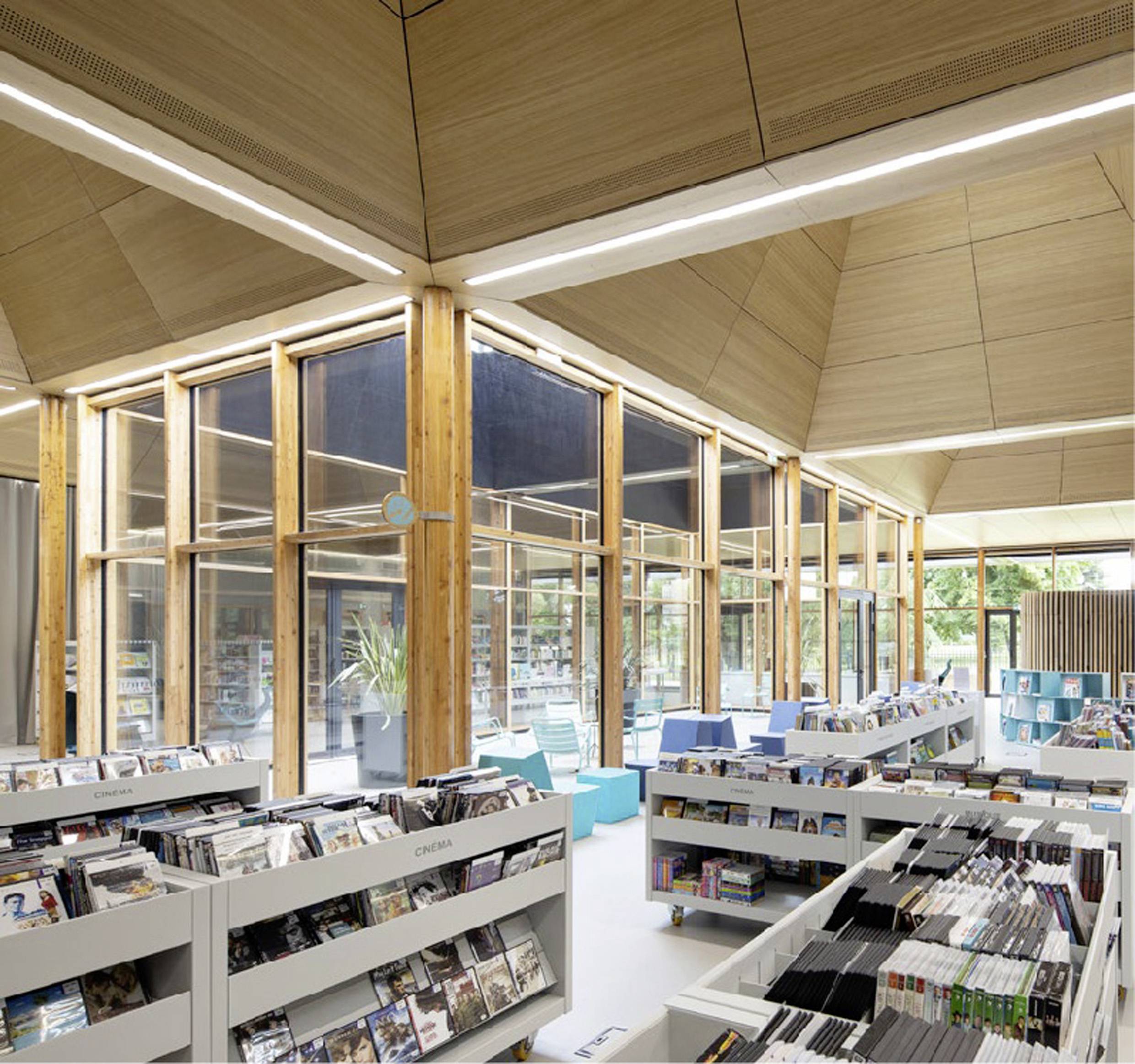 Een lichte, moderne bibliotheekruimte met houten accenten. De boekenkasten zijn gevuld met boeken en media. Grote ramen zorgen voor daglicht.