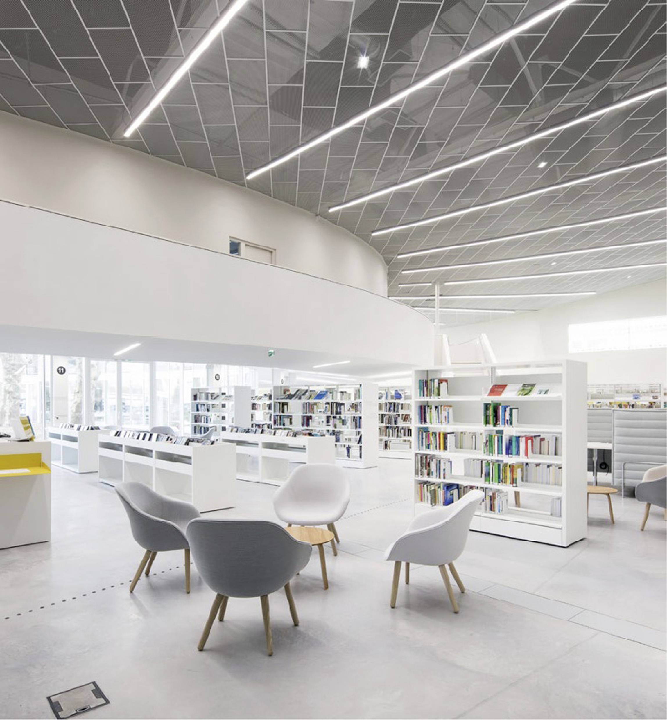 Lichte, moderne bibliotheek met witte boekenkasten, ronde zitplaatsen en grote ramen die veel natuurlijk licht binnenlaten.
