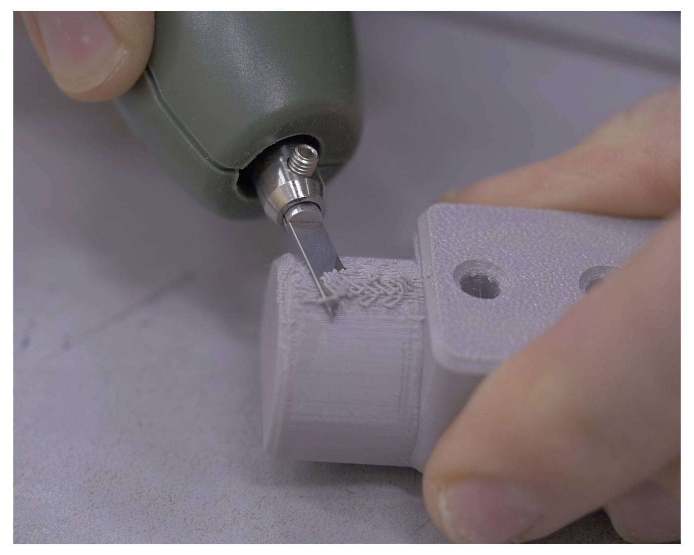 Een persoon gebruikt een precisiegereedschap om een 3D-geprint onderdeel te snijden of te verfijnen, waarbij een handmatig afwerkingsproces wordt gedemonstreerd op een object met gaten.