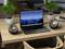 Een laptop op een houten tafel toont een bergachtergrond op het scherm. Ernaast staan twee speakers en drie potplanten.