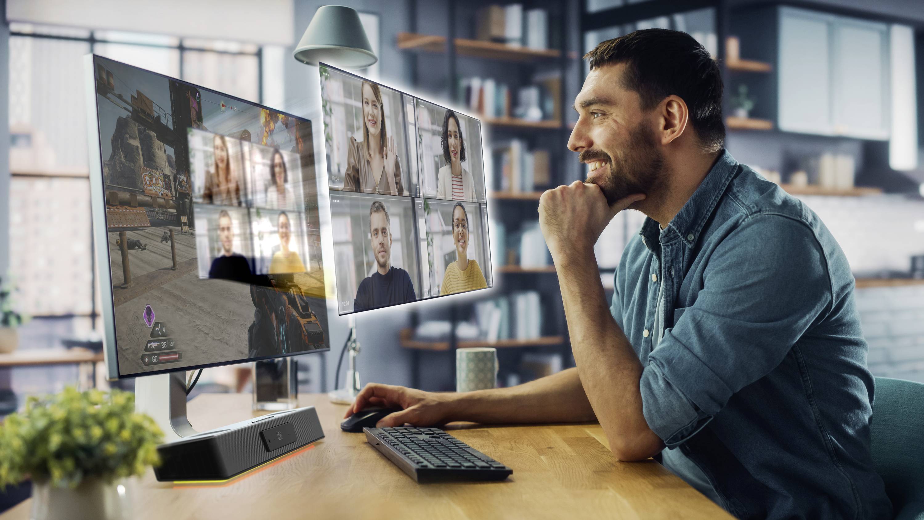 Een man zit aan een bureau met twee monitors. Op het ene scherm is een videospel te zien, op het andere een videoconferentiegesprek.