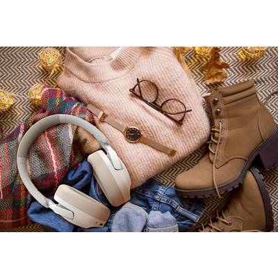 Trui, bril, horloge, koptelefoon, laarzen en sjaal liggen op een deken. Herfstelijke sfeer met warme kleurtinten en gezellige accessoires.