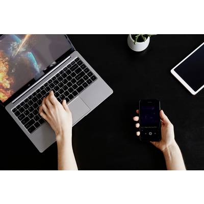 Een persoon typt op een laptop terwijl hij/zij een smartphone in de andere hand vasthoudt. Een tablet ligt naast de laptop op tafel.