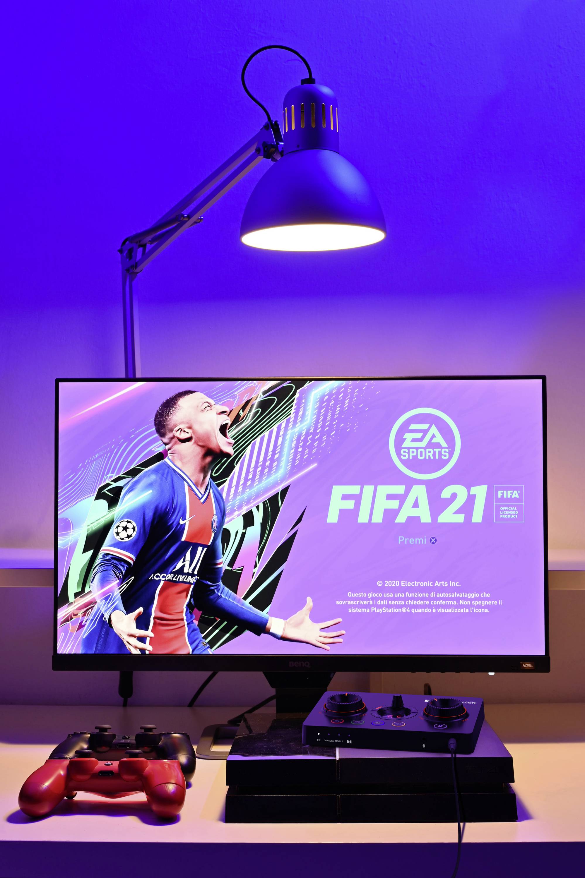 Een computerscherm toont het startscherm van 'FIFA 21' met een juichende voetballer. Een controller ligt ernaast.