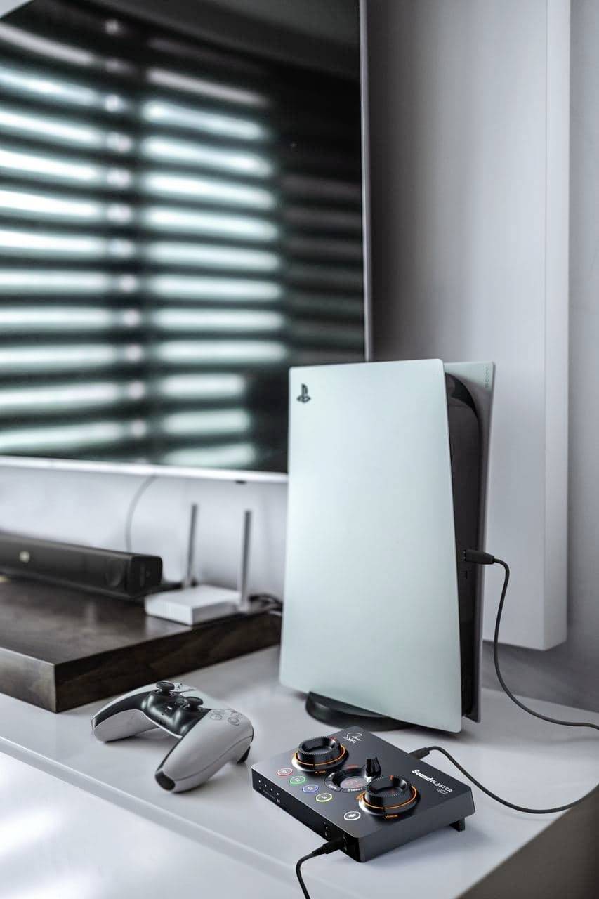 Een modern game console-setup met een console, een controller en een audiomixer op een tafel in een lichte ruimte.