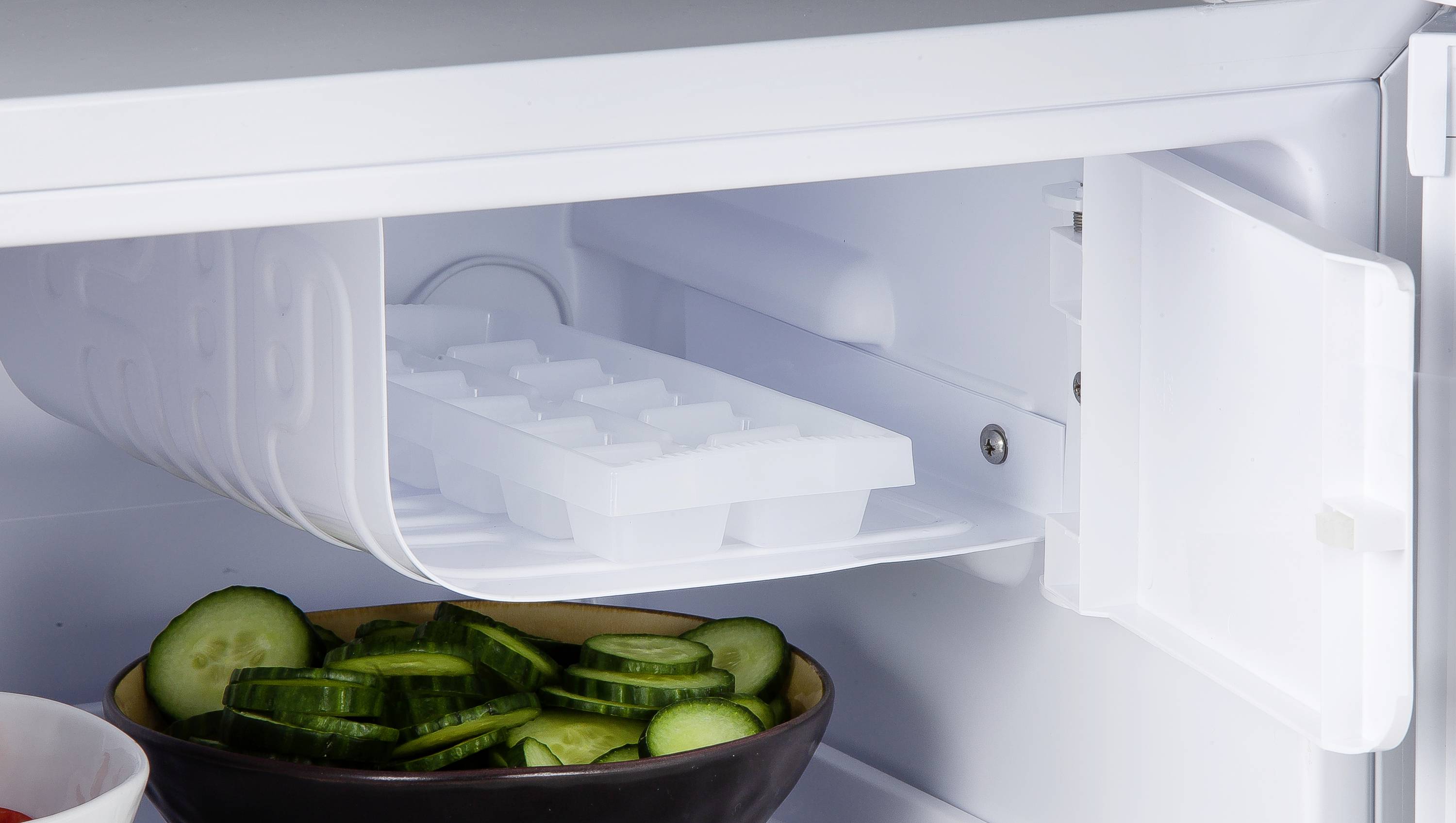 Een openstaande koelkast met een compartiment voor ijsblokjes en een bakje met gesneden komkommers.