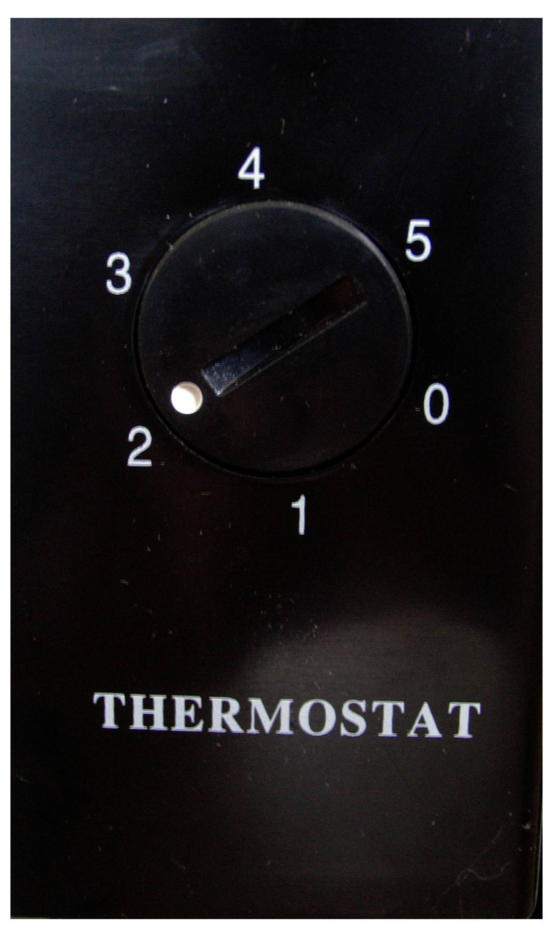 Een zwart thermostaat met een schaal van 0 tot 5; de pijl wijst naar 1. Eronder staat het woord 'THERMOSTAAT'.