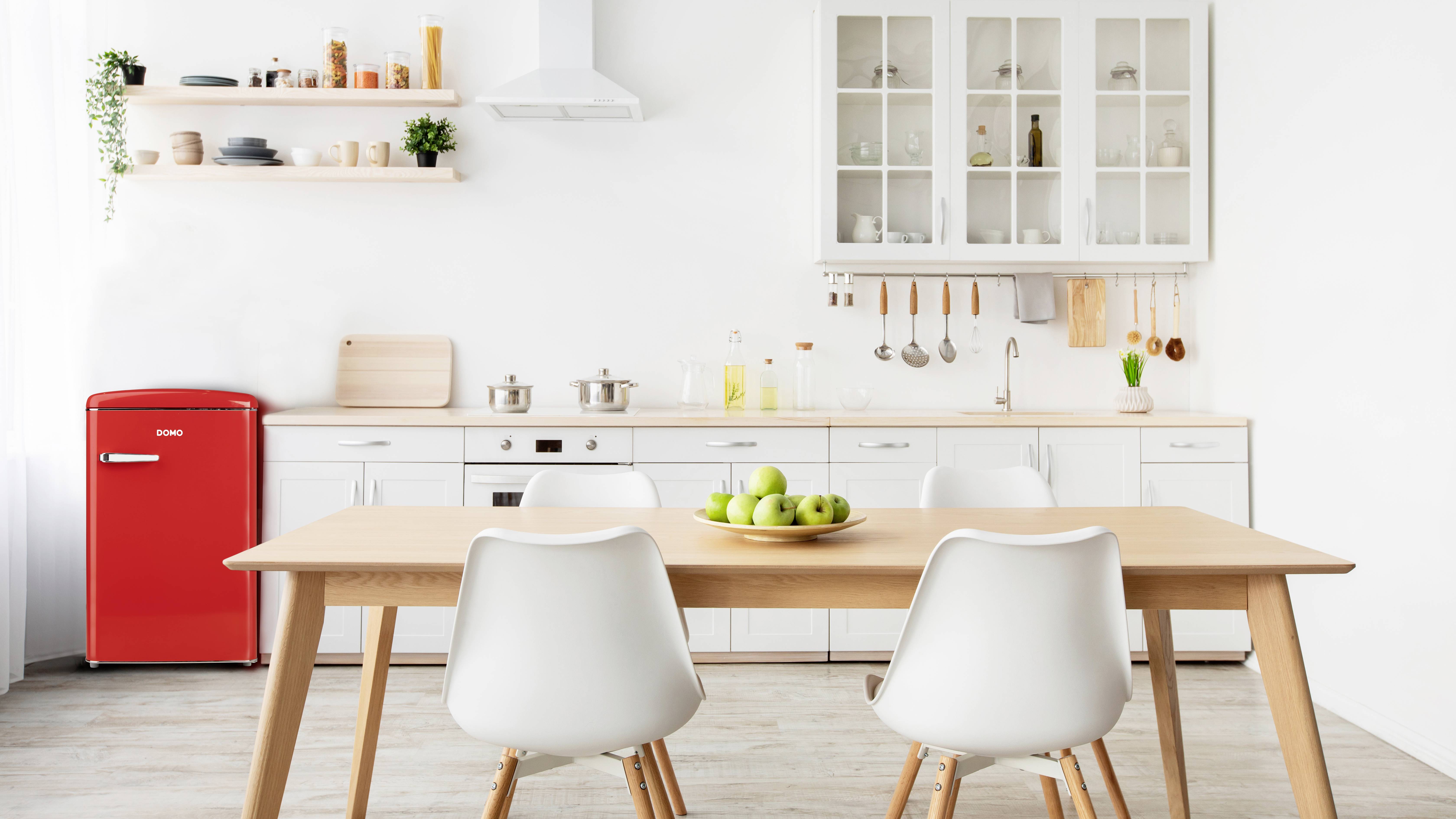 Moderne keuken met houten tafel en vier stoelen, rode retro-koelkast en witte kasten. Tafel met schaal vol groene appels.